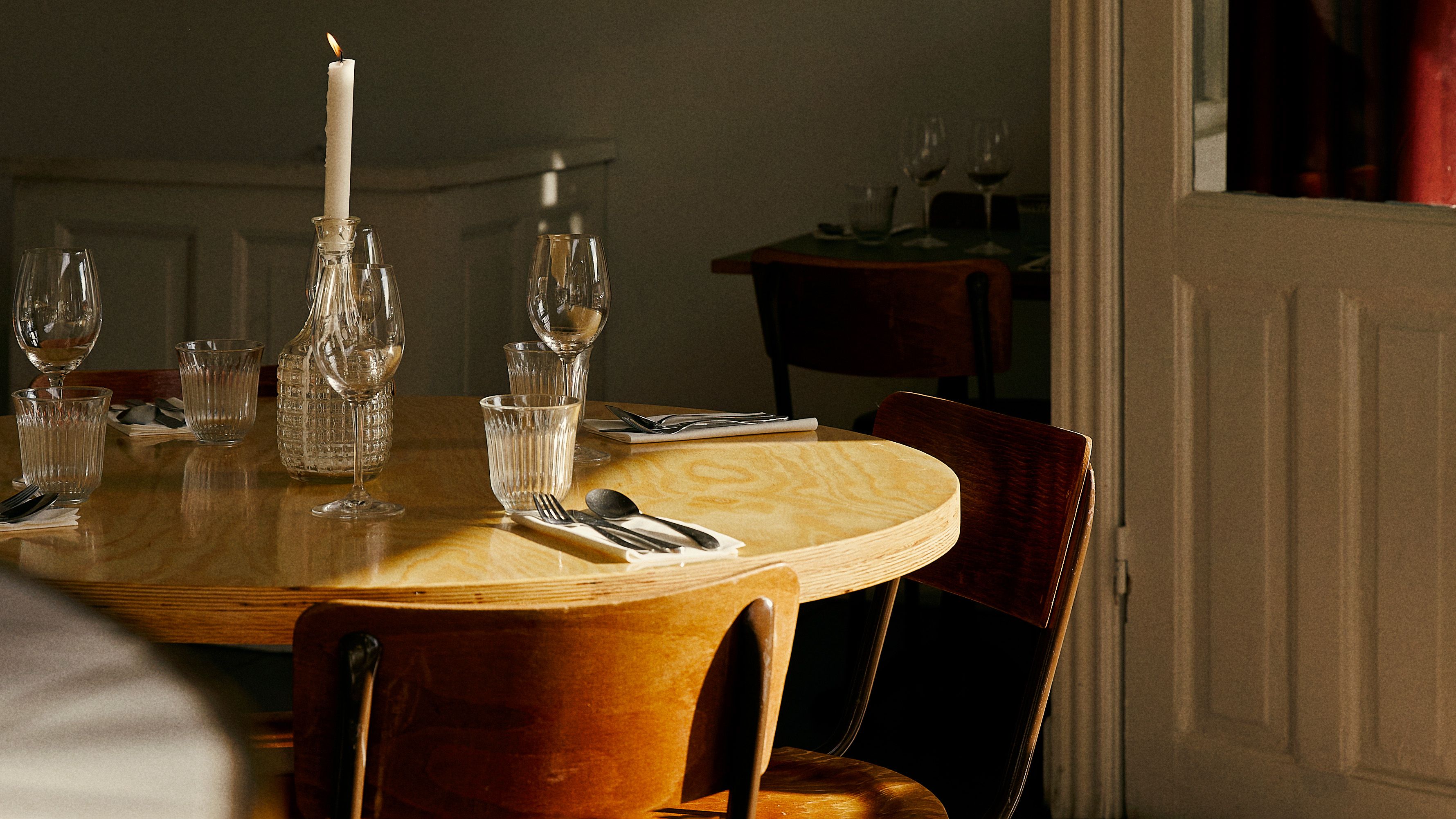Rundt bord med to stole og en lysestage med et stearinlys og forskellige glas og bestik.