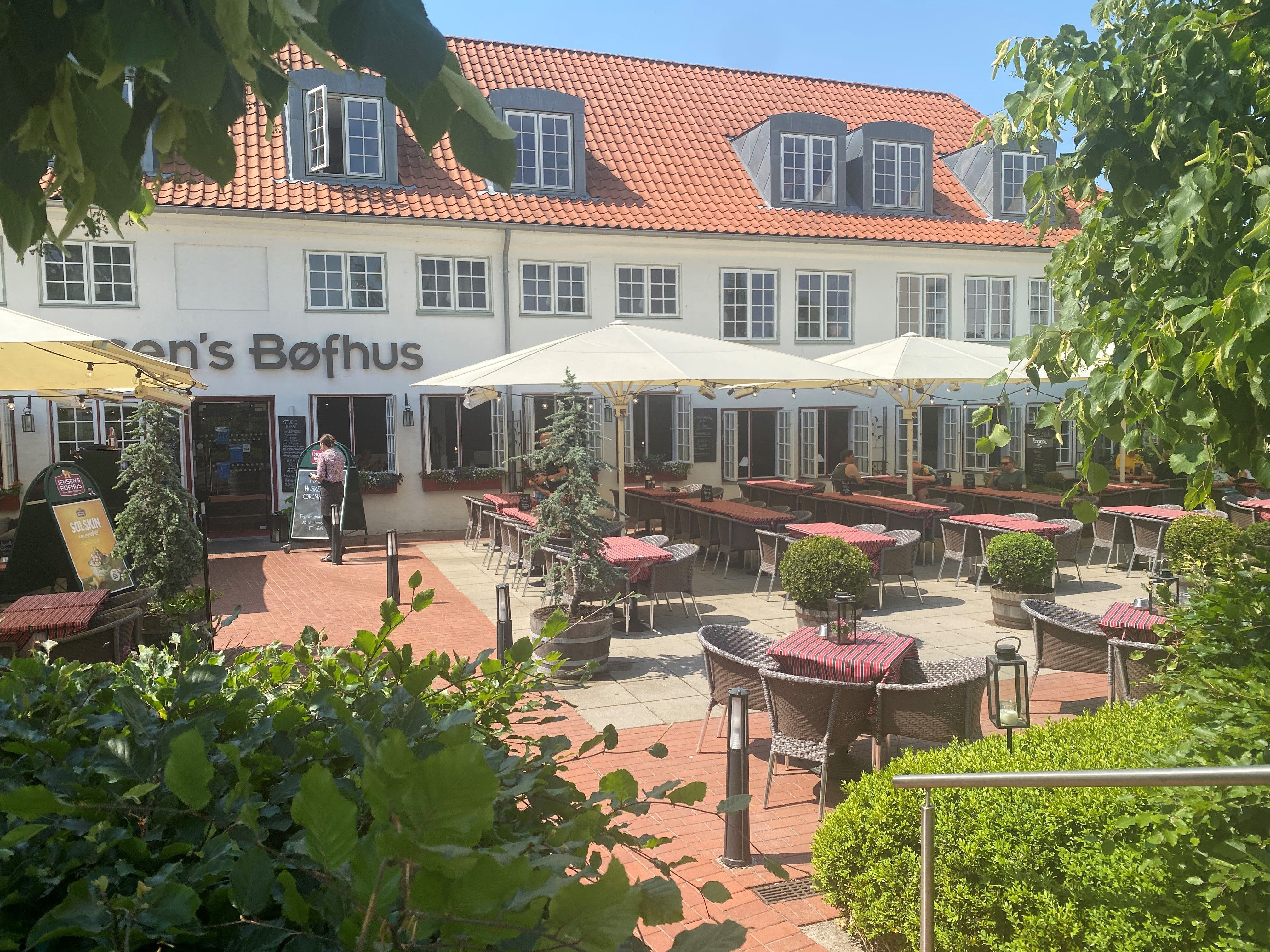 Terrasse med bord og stole på et café, restaurantområde med en række plantepoteter og parasoller