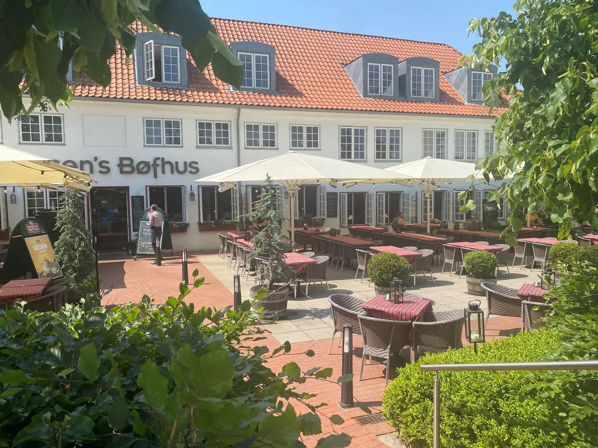 Terrasse med bord og stole på et café, restaurantområde med en række plantepoteter og parasoller