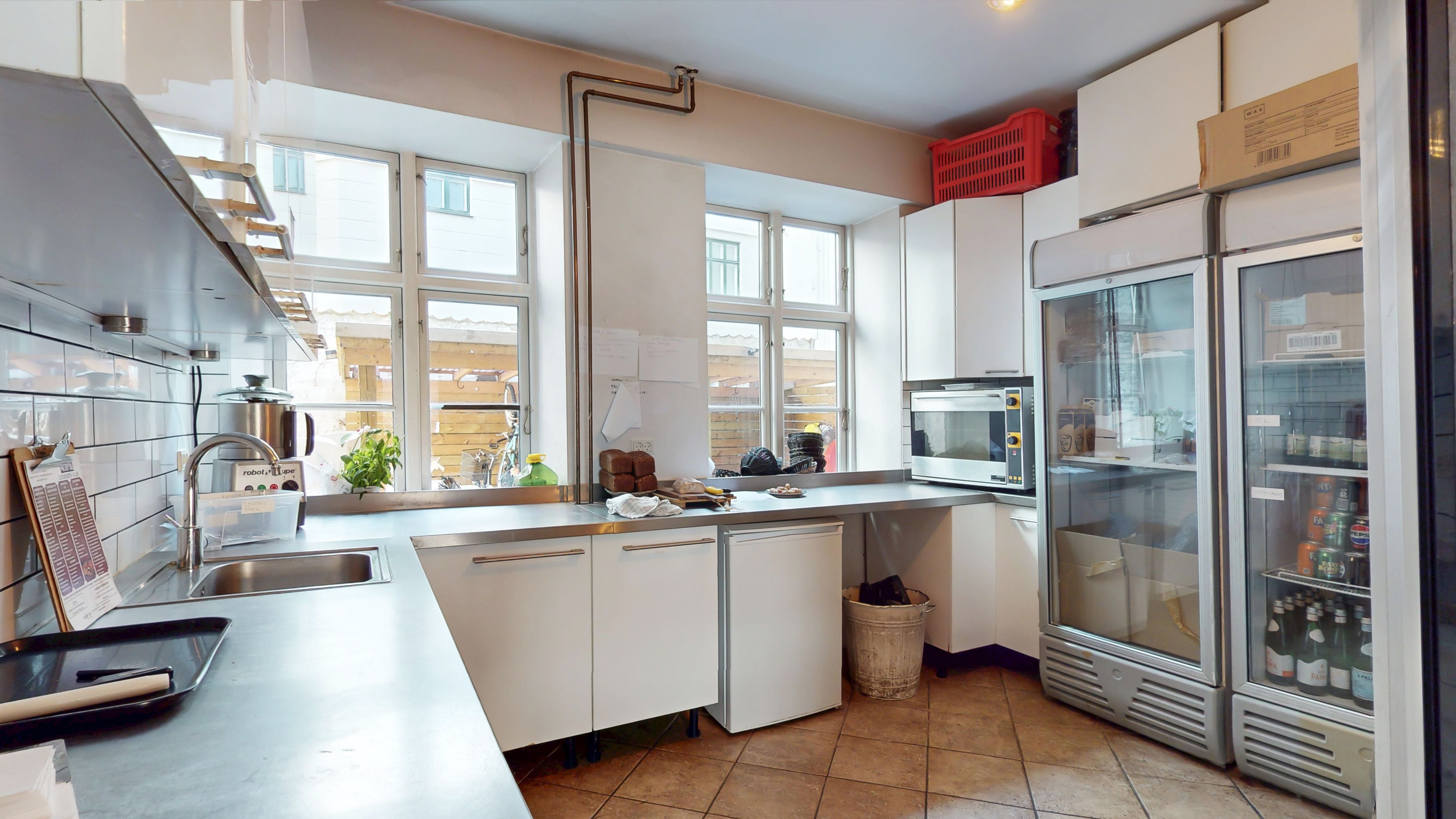 En stor køkken i en lejlighed med to køleskabe, et vaskebækken, to køkkenhylder, en mikroovn, et køkkenbord og et vindue med udsigt til gaden