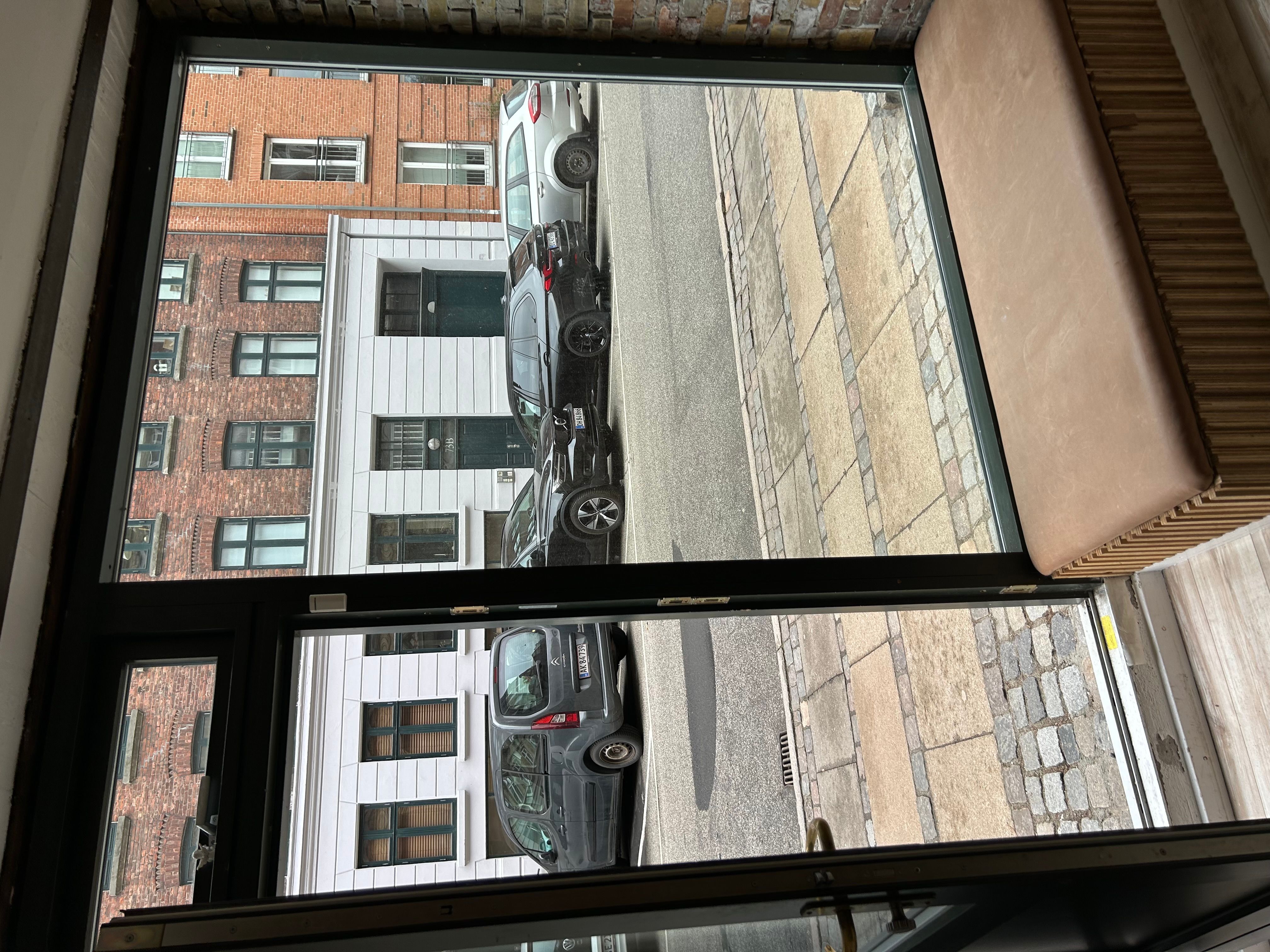 En lejlighed med udsigt til Ryesgade 72 i København Ø. Udenfor ses tre parkerede biler og en terrasse med udsigt til en brostensbelagt gågade.
