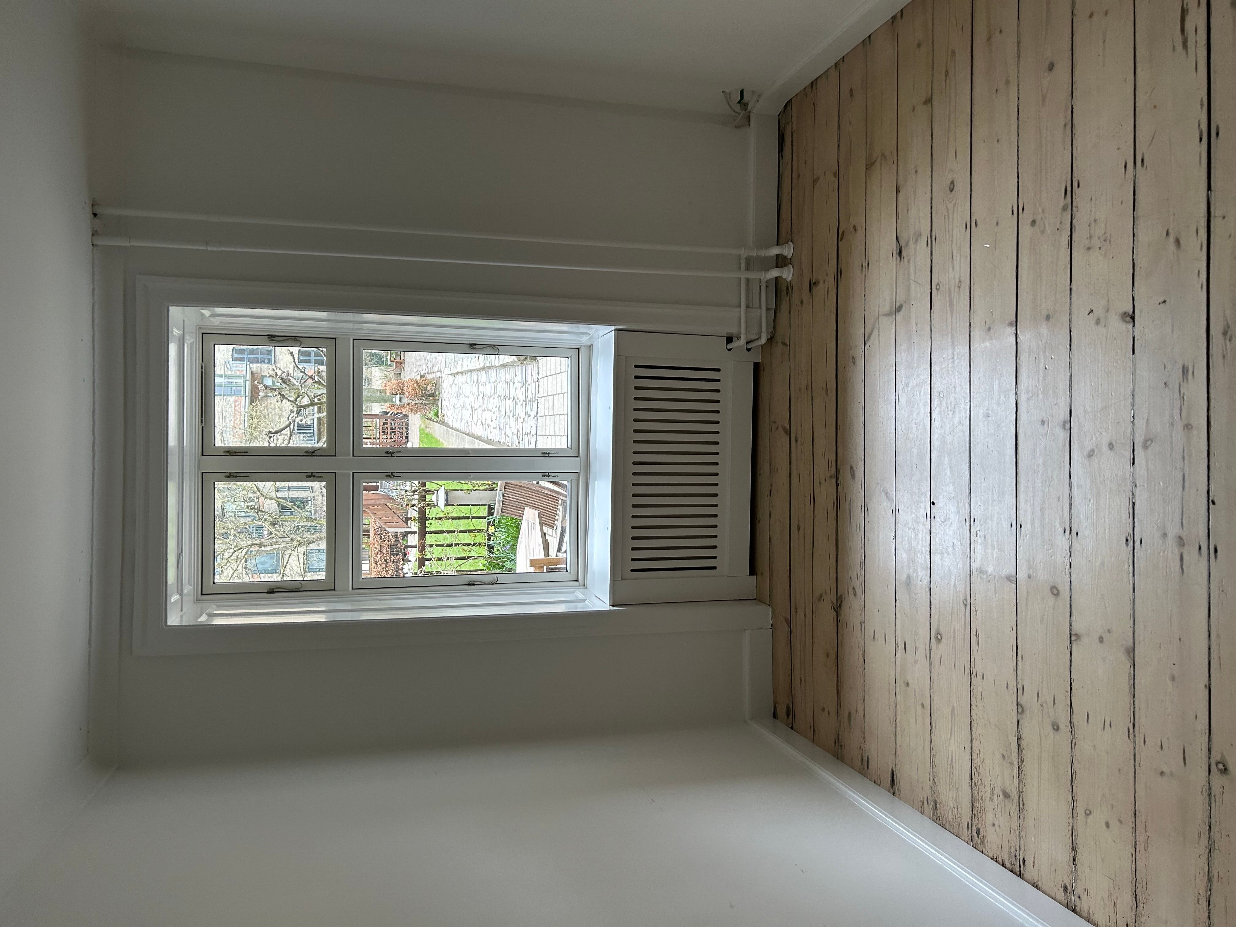 Indersiden af et kontorlokal med hvid væg og loft, hvor der er slanke hvide ruder med udsigt til grønne træer og en bygning med en terrasse