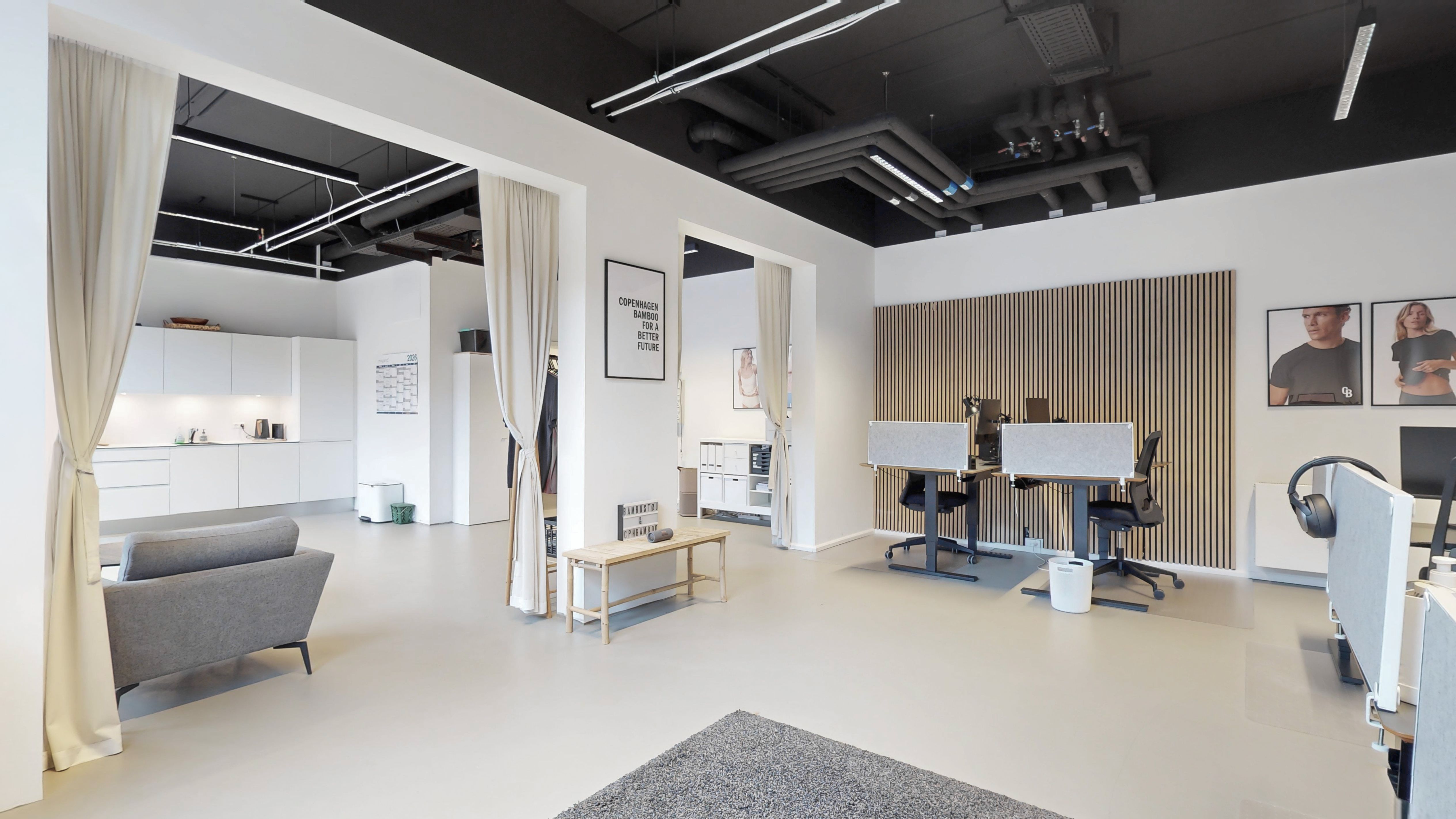 Lyst og moderne kontorlokale med lyse vægge og højloft. Hvidt køkken med lyse skuffer og slanke linjer. To smukke bordplader med moderne stolpe og lydisolering. Et moderne mødelokale med en sofa og et skrivebord.