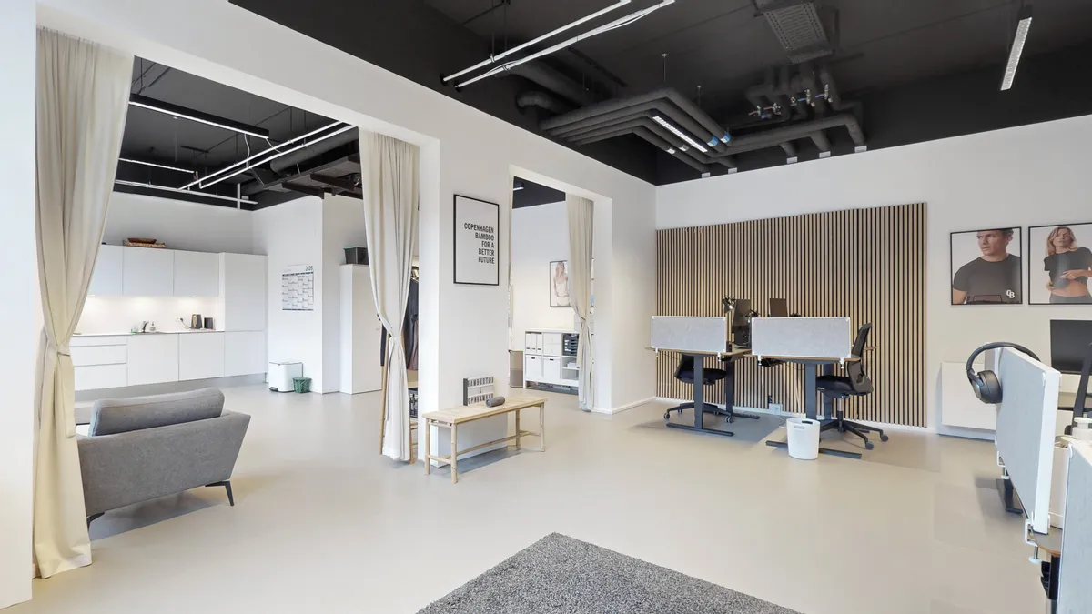 Lyst og moderne kontorlokale med lyse vægge og højloft. Hvidt køkken med lyse skuffer og slanke linjer. To smukke bordplader med moderne stolpe og lydisolering. Et moderne mødelokale med en sofa og et skrivebord.