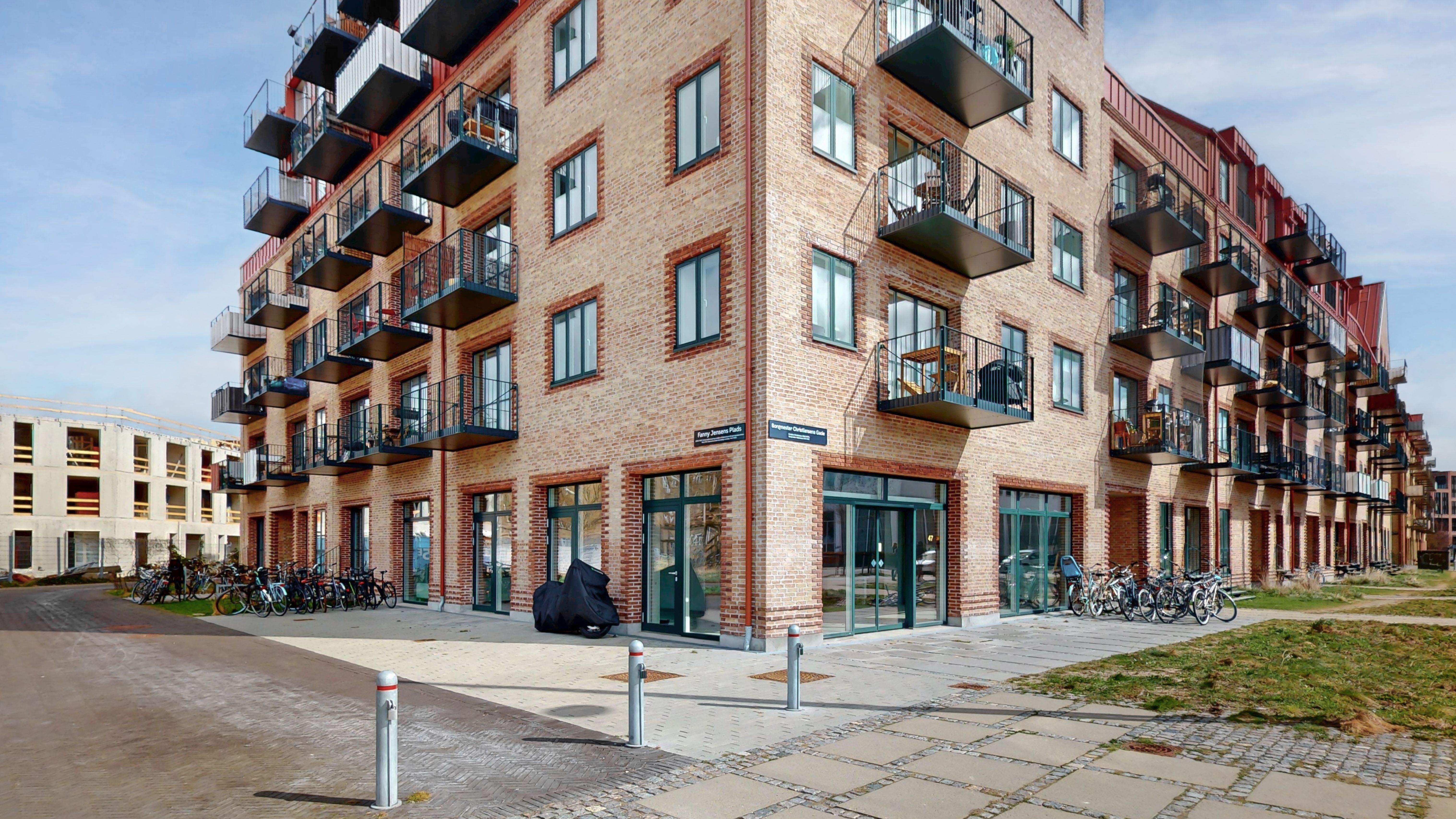 Nybygget hjørnelejemål i Sydhavn med terrasser og glasdøre. Lejlighedsbygning med moderne interiør. Parkerede cykler og grønne områder. Moderne arkitektur med tegl og glas.