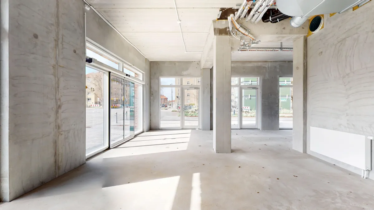 Et nybygget erhvervslejemål i Sydhavn med hjørnebeliggenhed og glasdøre og -ruder. Lejemålet med eksponeret beton og et lyse gulv.