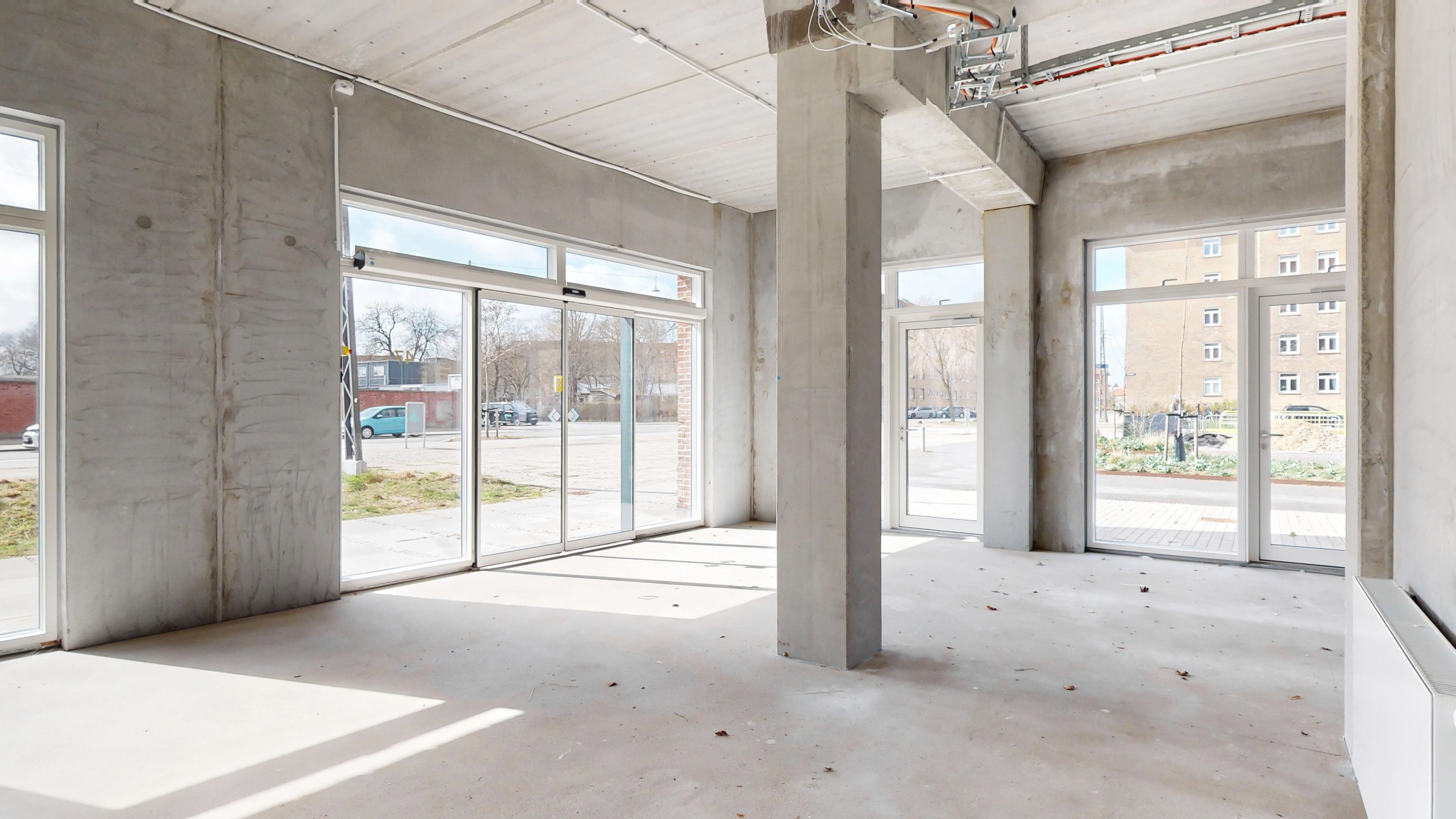 Et stort rum med hvide vægge og glasdøre samt større glasruder og gulv. Lejemålet er placeret i Sydhavn. Der er en bygning med flere vinduer i baggrunden.