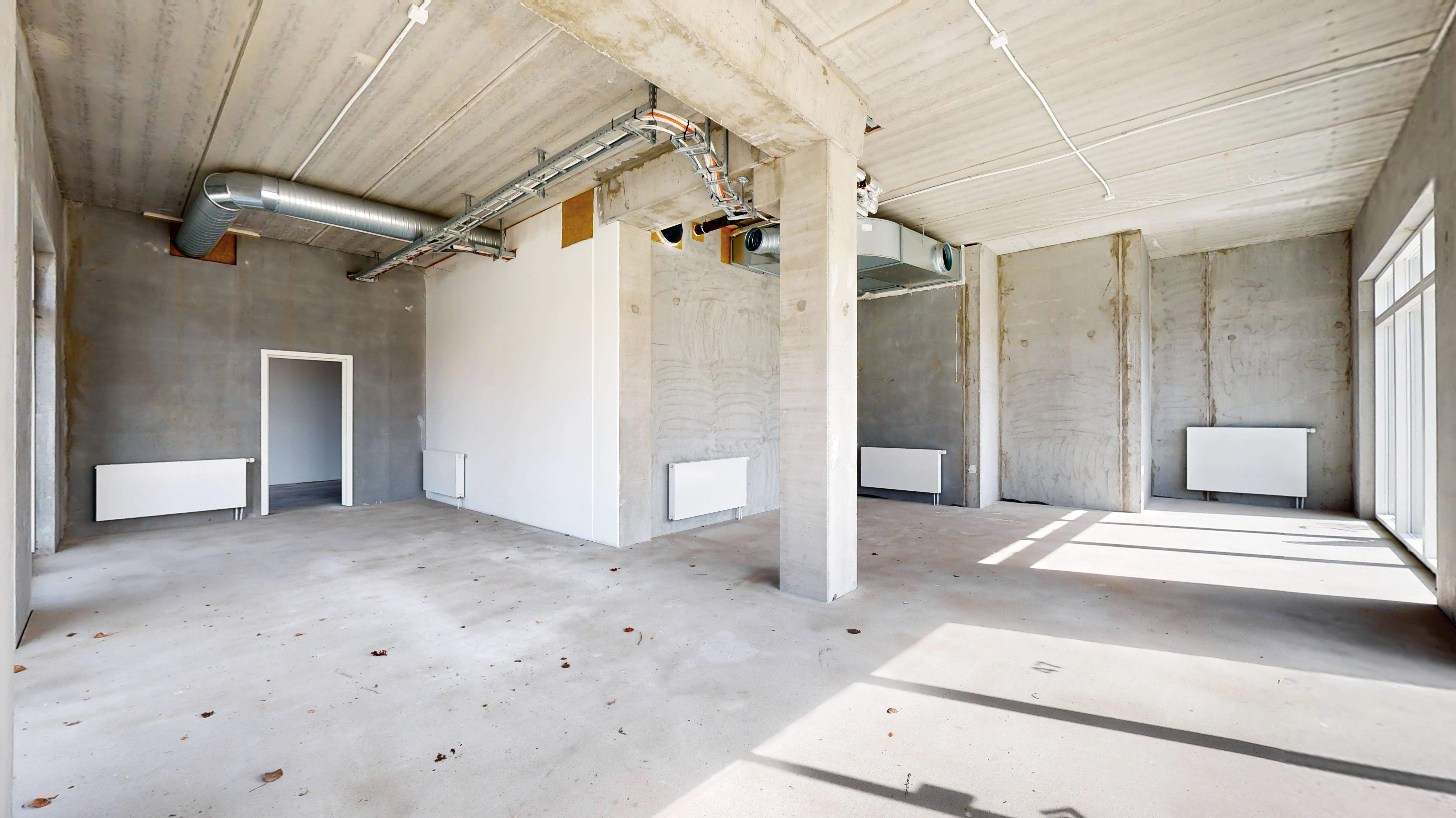 En nyopført hjørnebygning med rå gulv, hvide vægge og to hvide radiatorer, et skråt gulv og en støbejernshjørnebjælke