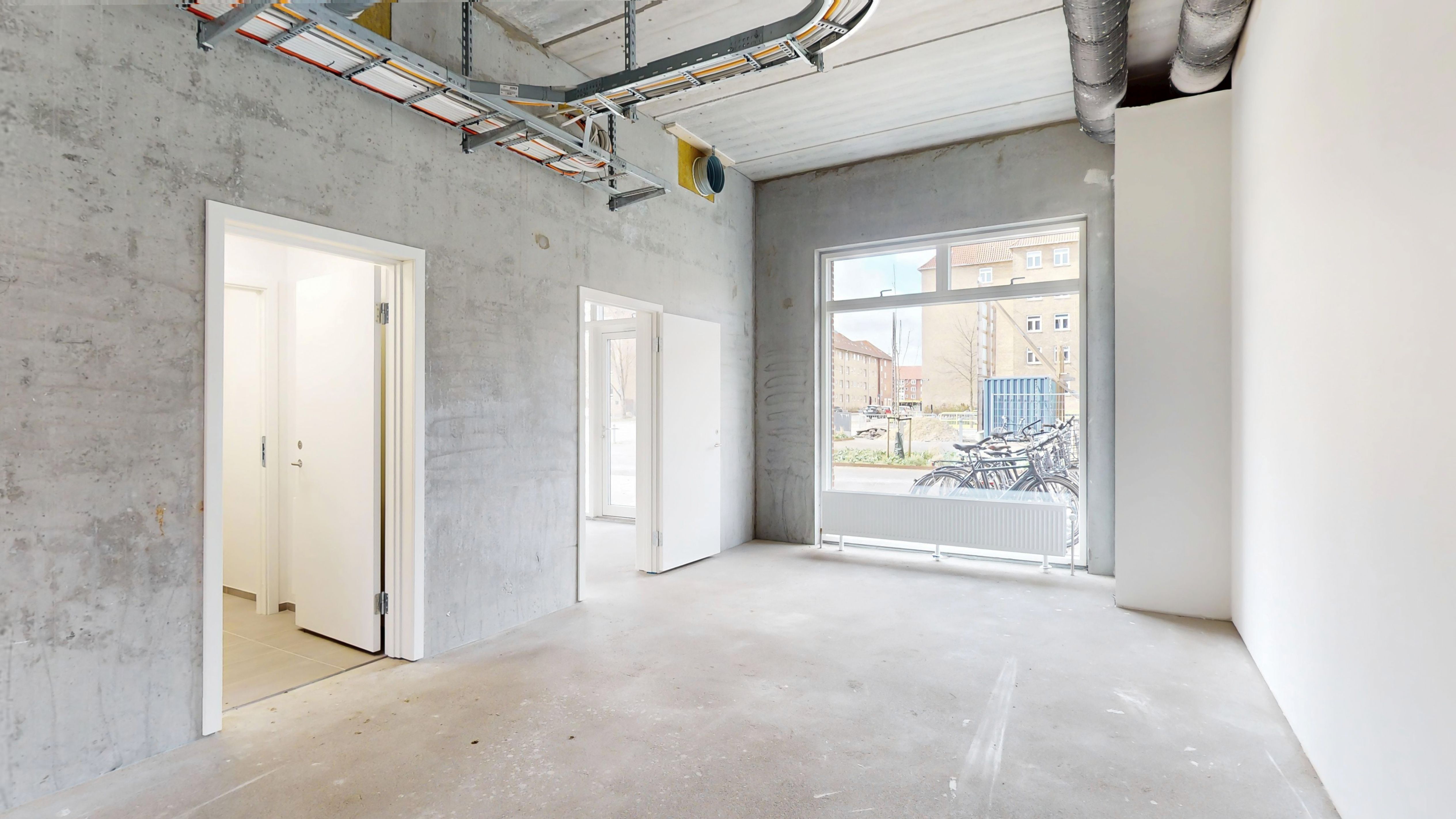 Rummeligt og åbent lokale med hvidt loft og vægge, vinduer og højt hjørne. Døråbninger og radiatorer er installeret. Lejemål med hjørnebeliggenhed.