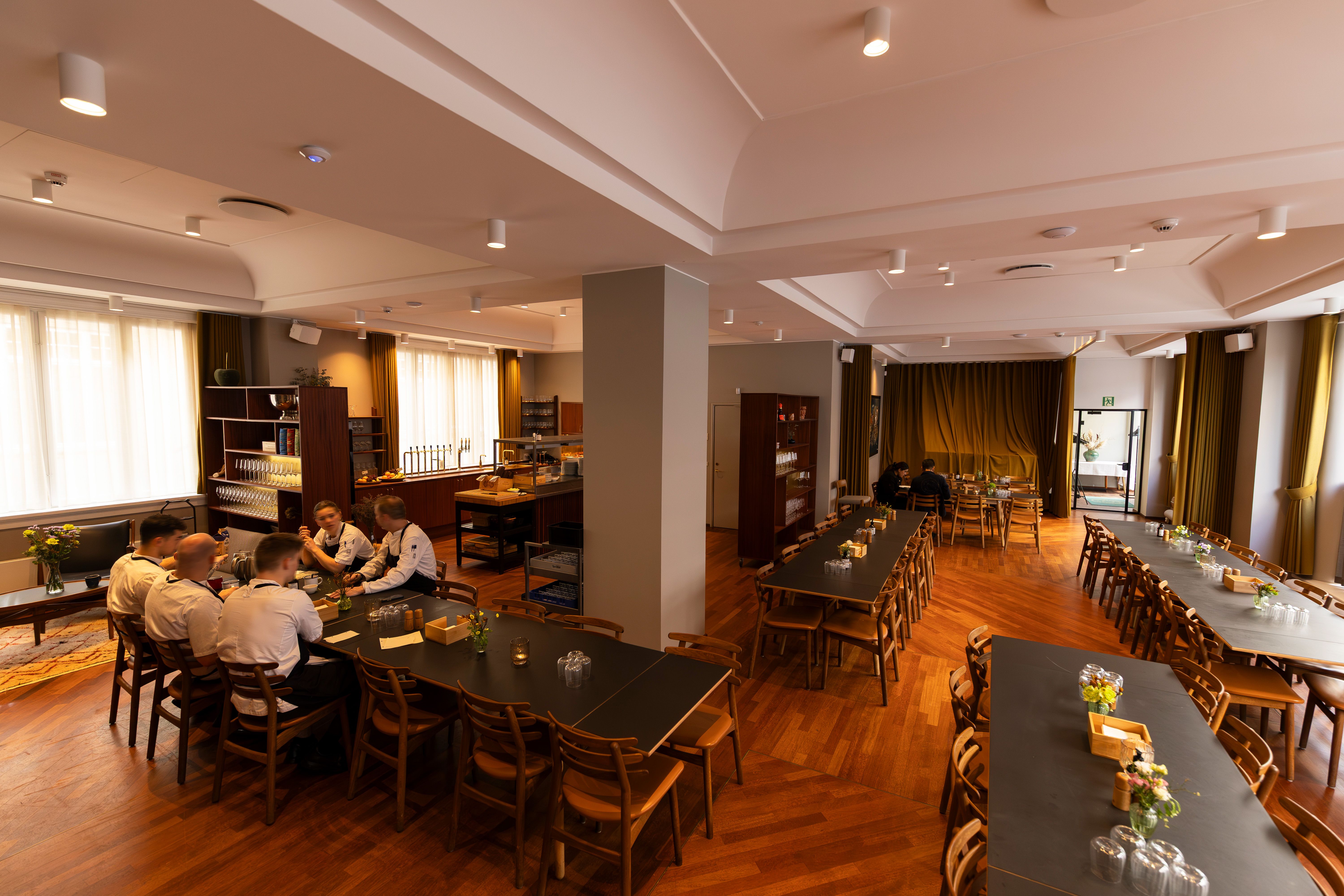 Mange mennesker i uniformer sammen med nogle blomster og glas på bordene i et luksuriøst kontormiljø i København