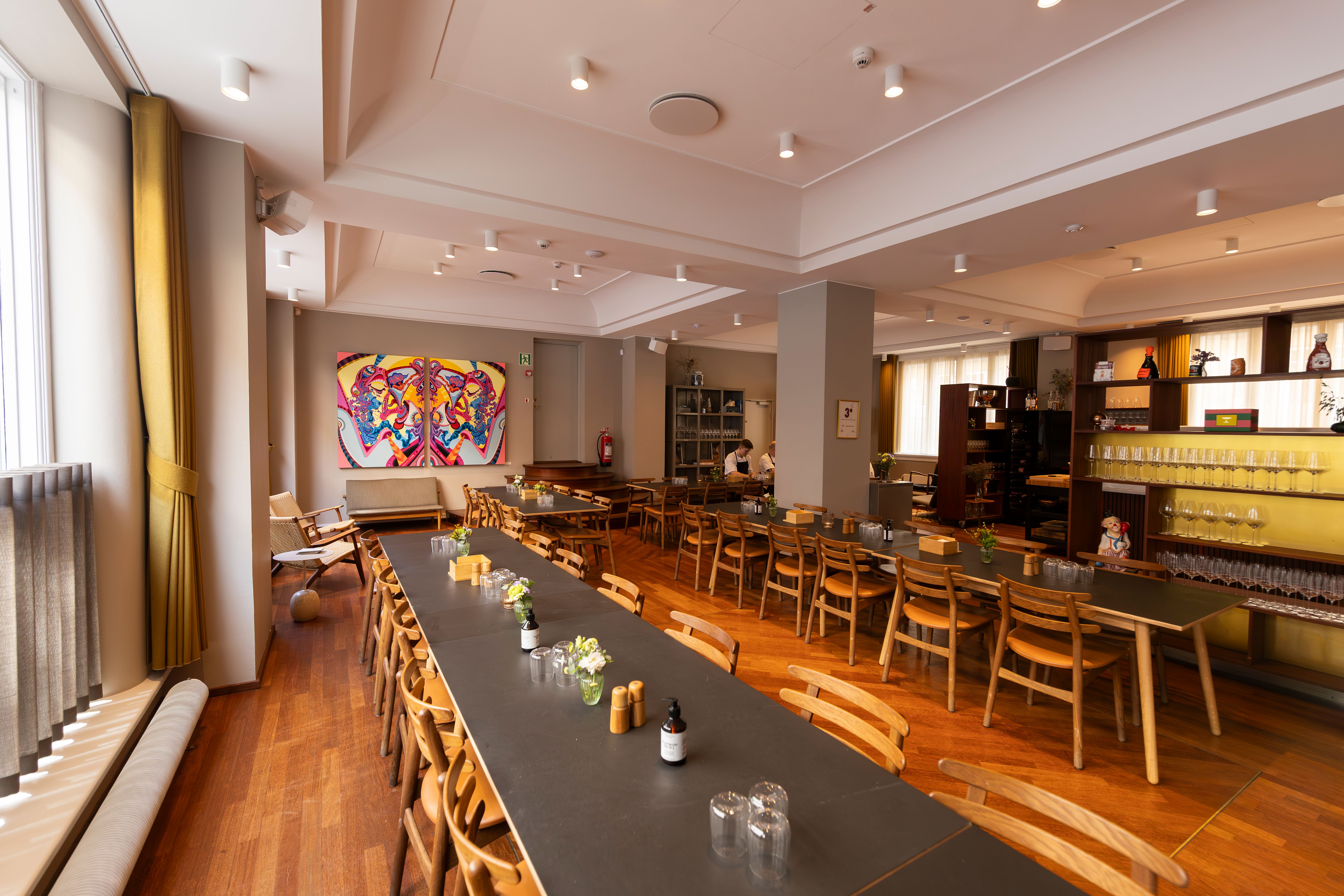 Indkvartering til leje i eksklusivt kontormiljø med lyse møbler og moderne indretning. Maleri på væggen og eksklusivt glaskabiner med vinglas.