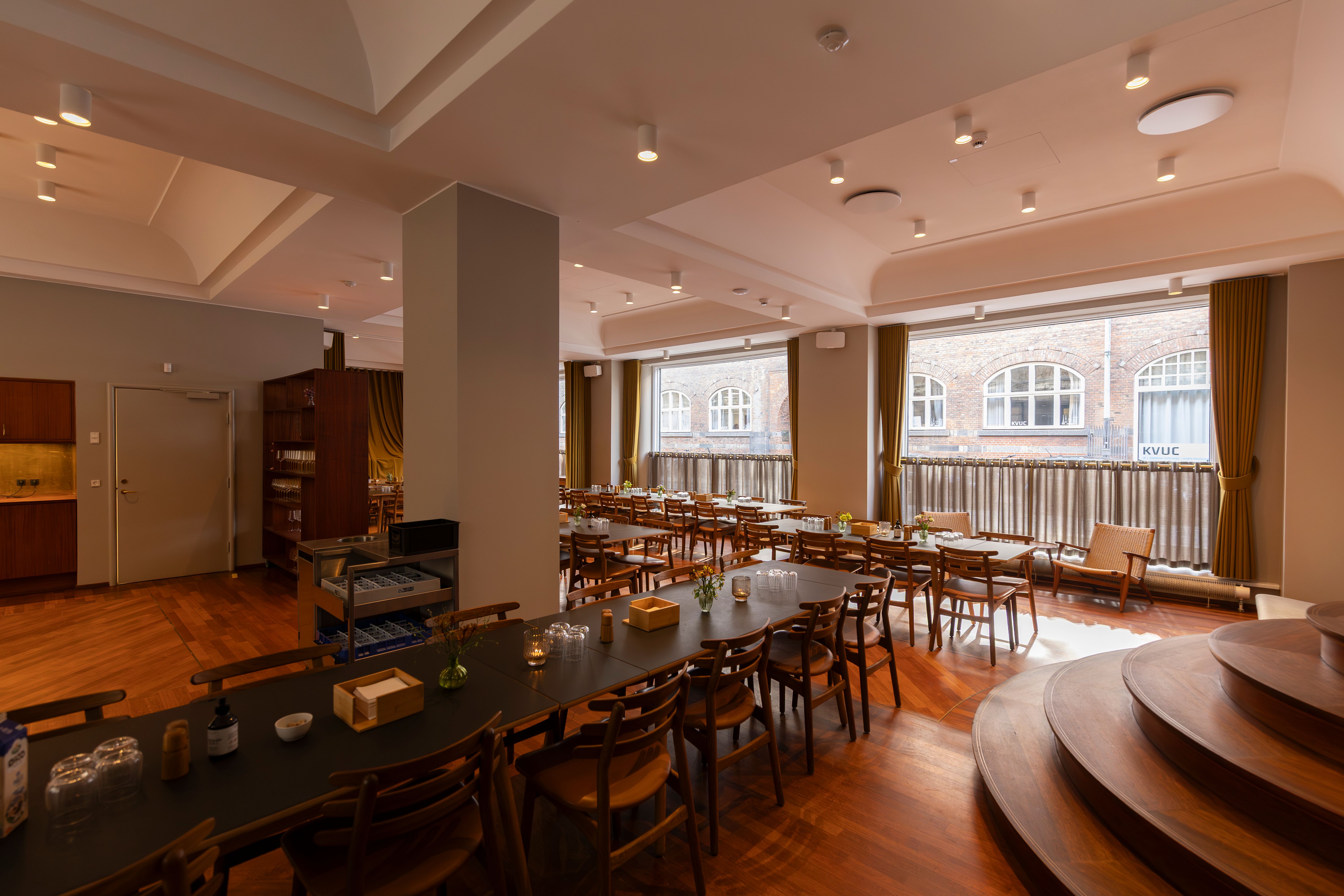 Moderne, lyse kontorlokaler med lyse trægulve og lysekroner, møbler og skriveborde samt store vinduer med udsigt til Kongens Have