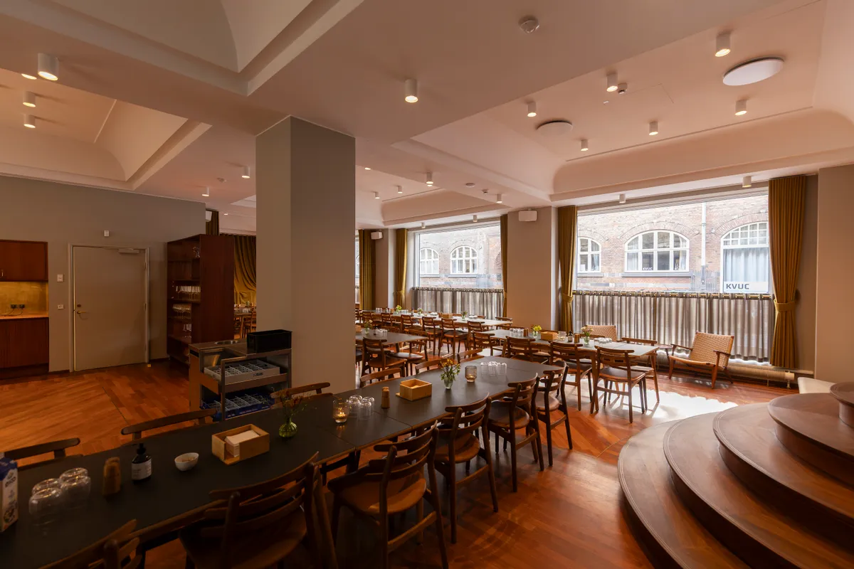 Moderne, lyse kontorlokaler med lyse trægulve og lysekroner, møbler og skriveborde samt store vinduer med udsigt til Kongens Have