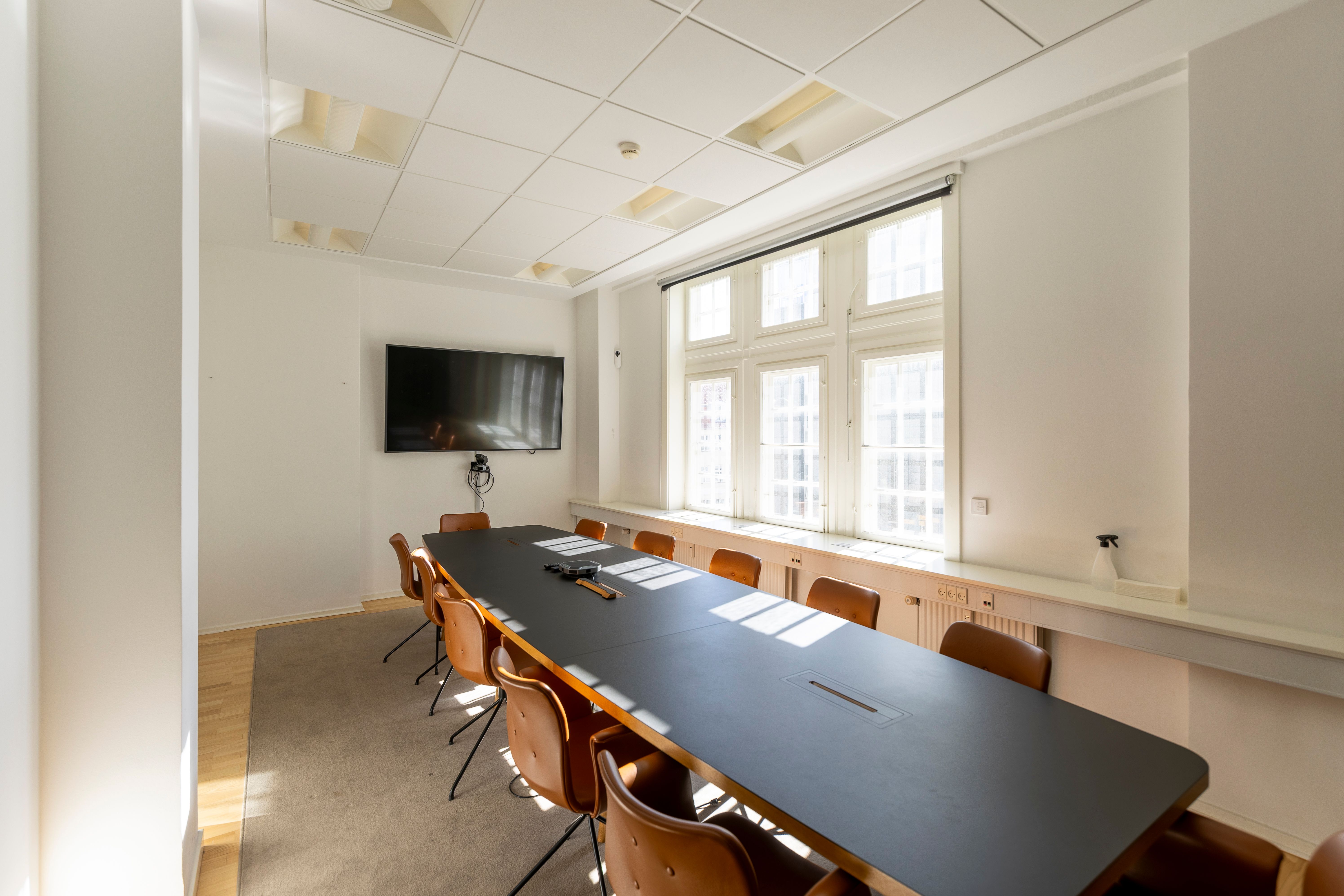 Ny kontor med lyse tage, tv, vinduer og borde samt stole med skinnende lædermøbler i lyse farver