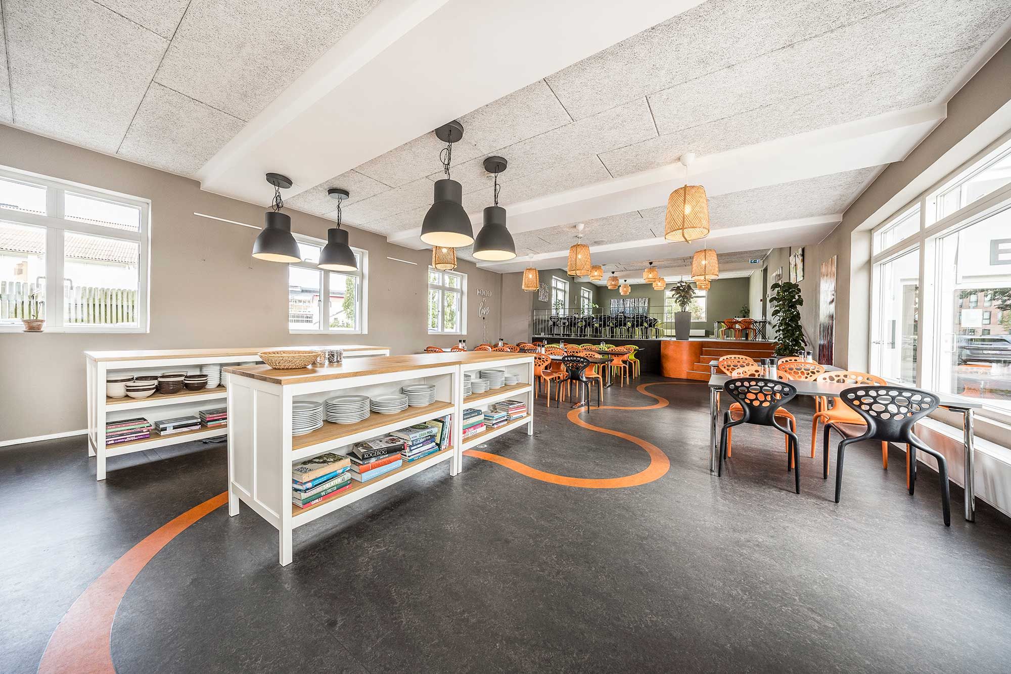 Kanteen med hvide vægge og orange gulv. Møbler og bøger på hylderne samt lysekroner og lampekugler på loftet