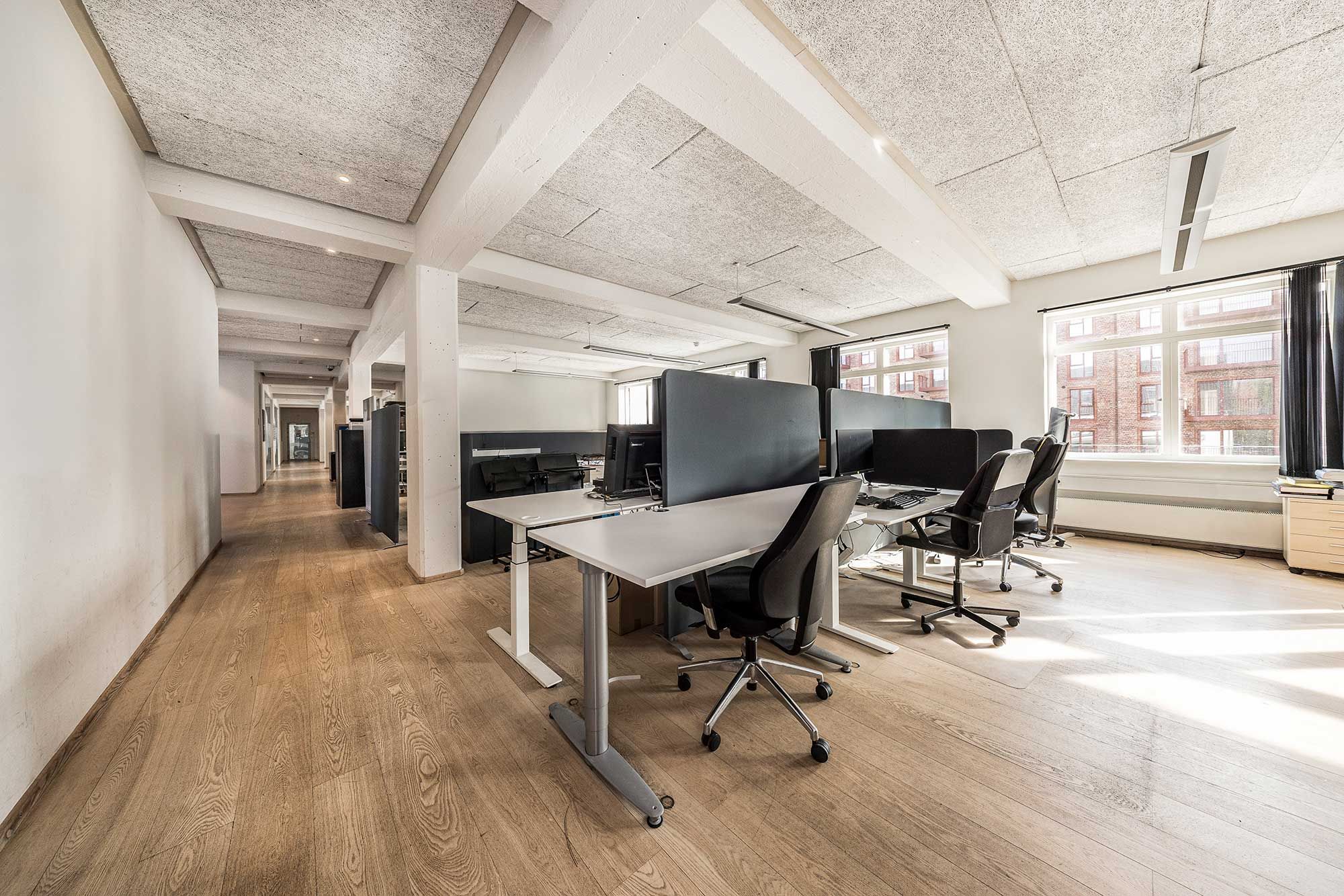 Kontor med højloft og lysevinduer, lysegulv, højteknologiske skriveborde og stolpe, samt lysanlæg. Her er plads til flere medarbejdere.