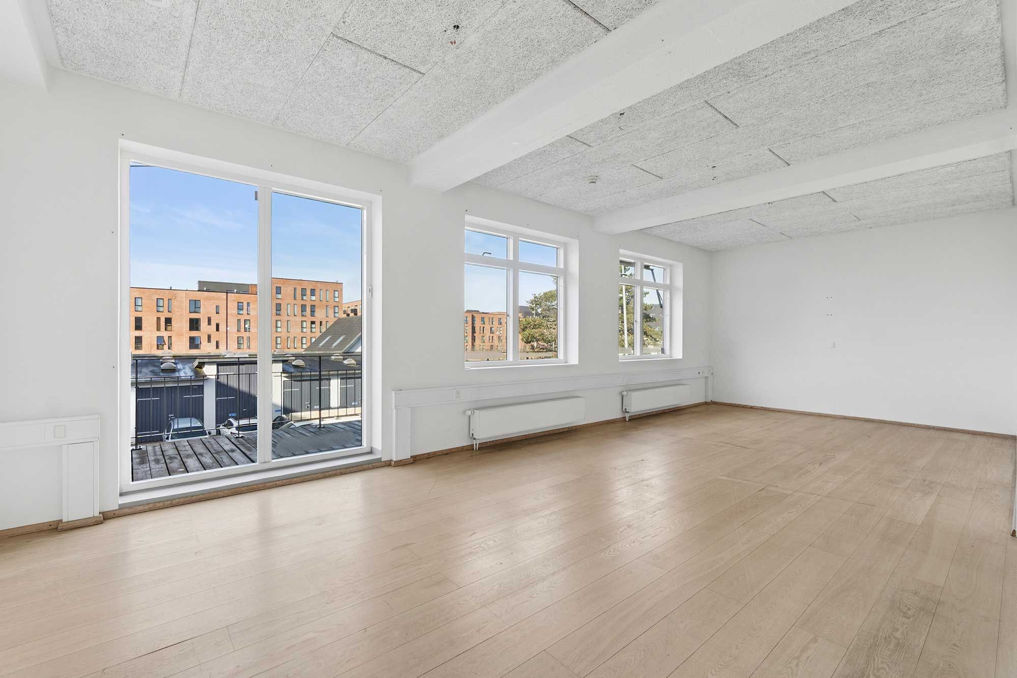 Rummelige kontorlokaler med hvidpudsede vægge, lyseglasvinduer og massivt trægulv. Køkken og fælles kantine. Udsigt over bygninger og vej.