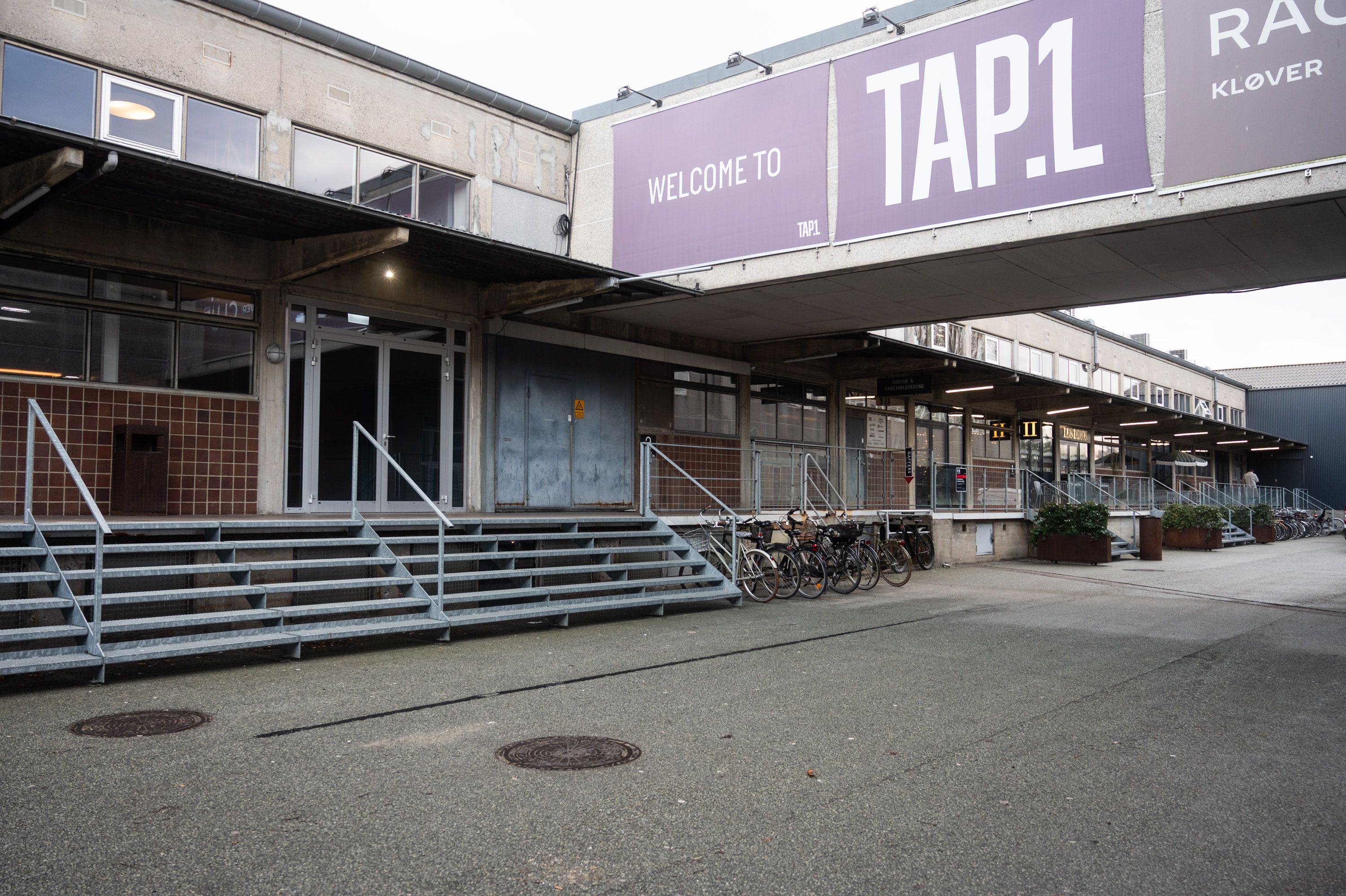 Udenfor er der et kontorbygger med skriften Welcome to Tap1 på facaden og flere cykler parkeret foran