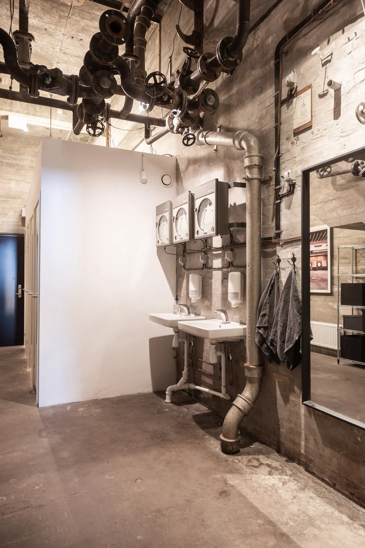 Håndvaskestativer med håndklæder og sæbeautomater, hængelig garderobe og røret system i loftet og på væggen i et renoveret loftsrum til leje i København