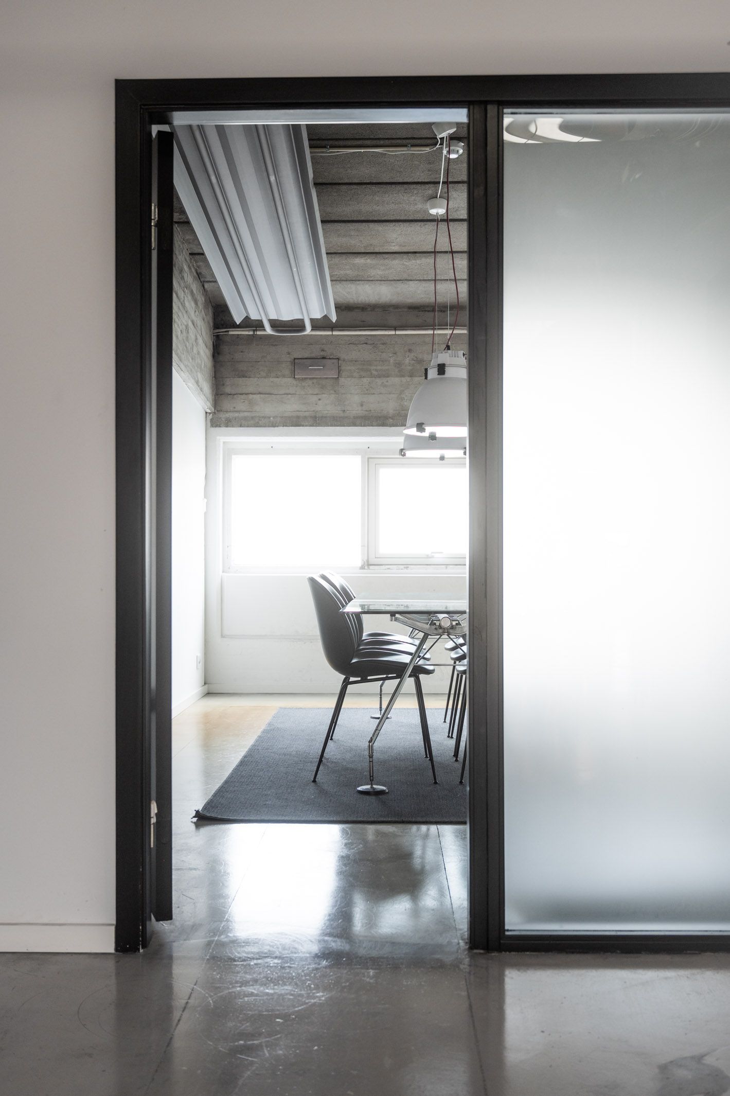 En moderne kontor med glasdør, højt loft og minimalistisk møbeldesign, hvor der er en bord med fire stole og to lysekroner