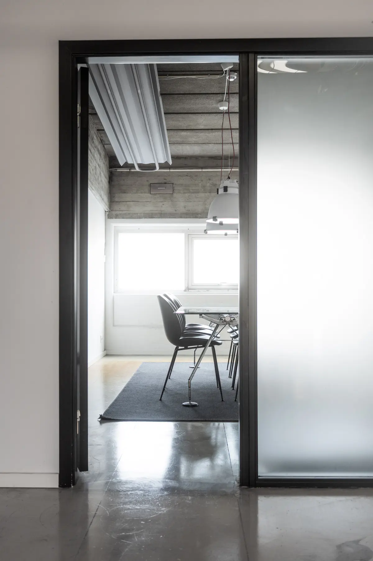 En moderne kontor med glasdør, højt loft og minimalistisk møbeldesign, hvor der er en bord med fire stole og to lysekroner