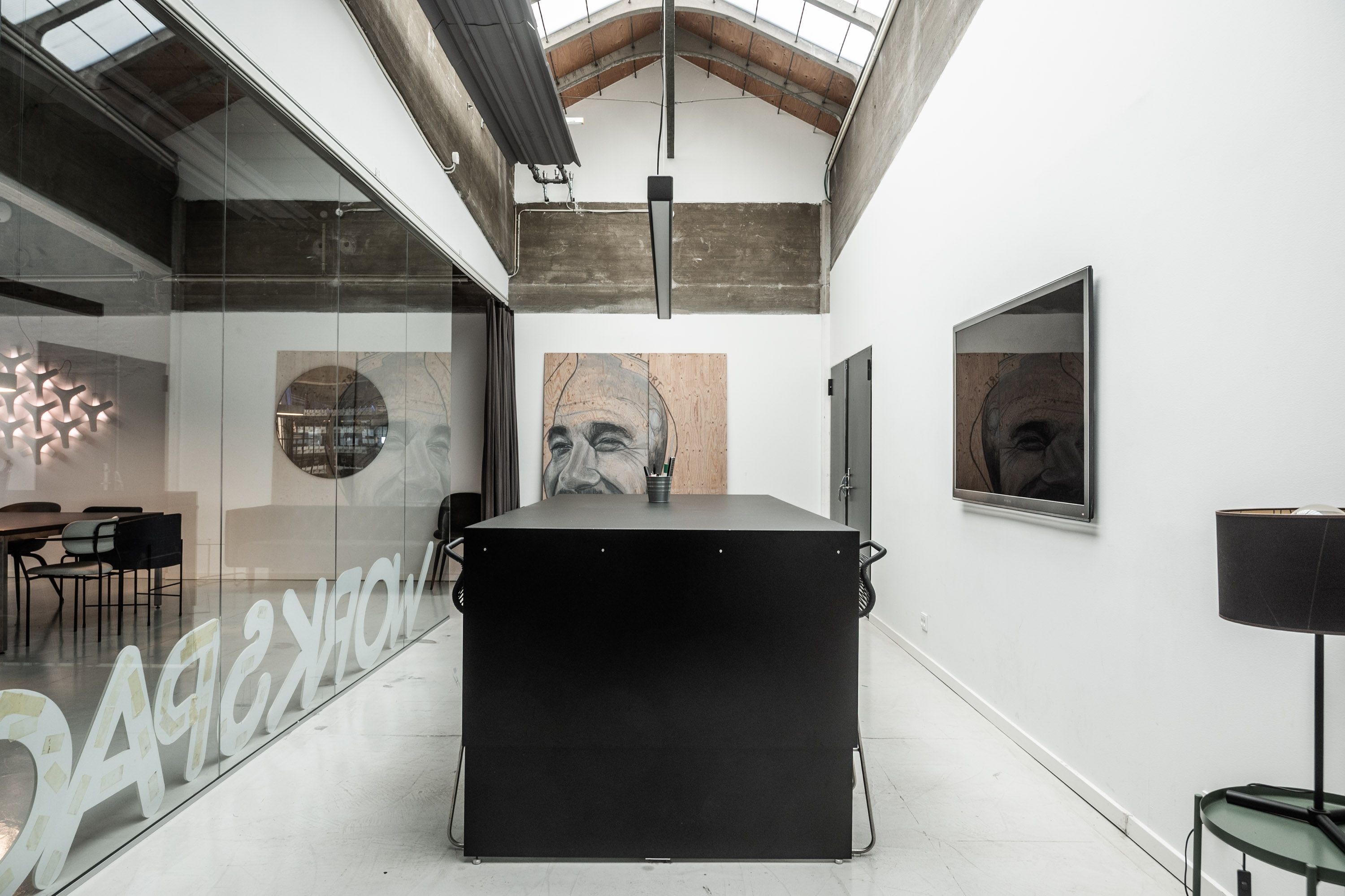 Et lille kontor med et bord og stole og tre malerier på væggen og glasruder og en lampeskærm