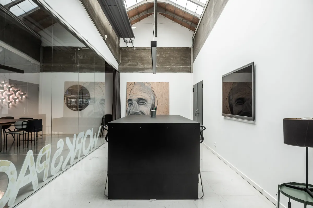 Et lille kontor med et bord og stole og tre malerier på væggen og glasruder og en lampeskærm