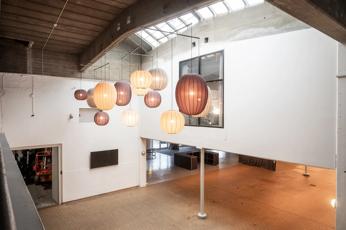 Rå industriloft med loftsvinduer og hængelampe. Loftsvinduer med gitter. Hvid væg med lys og hængelampe. Gulvtæppe med møbler og køretøj.