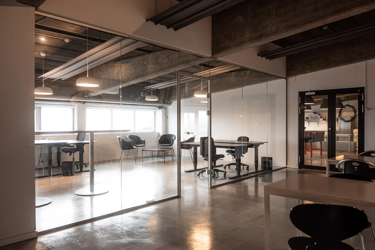 Glassvægge i det moderne og minimalistiske kontor med højt til loftet, hvide bord og stole, hængende lamper og åbent gulv