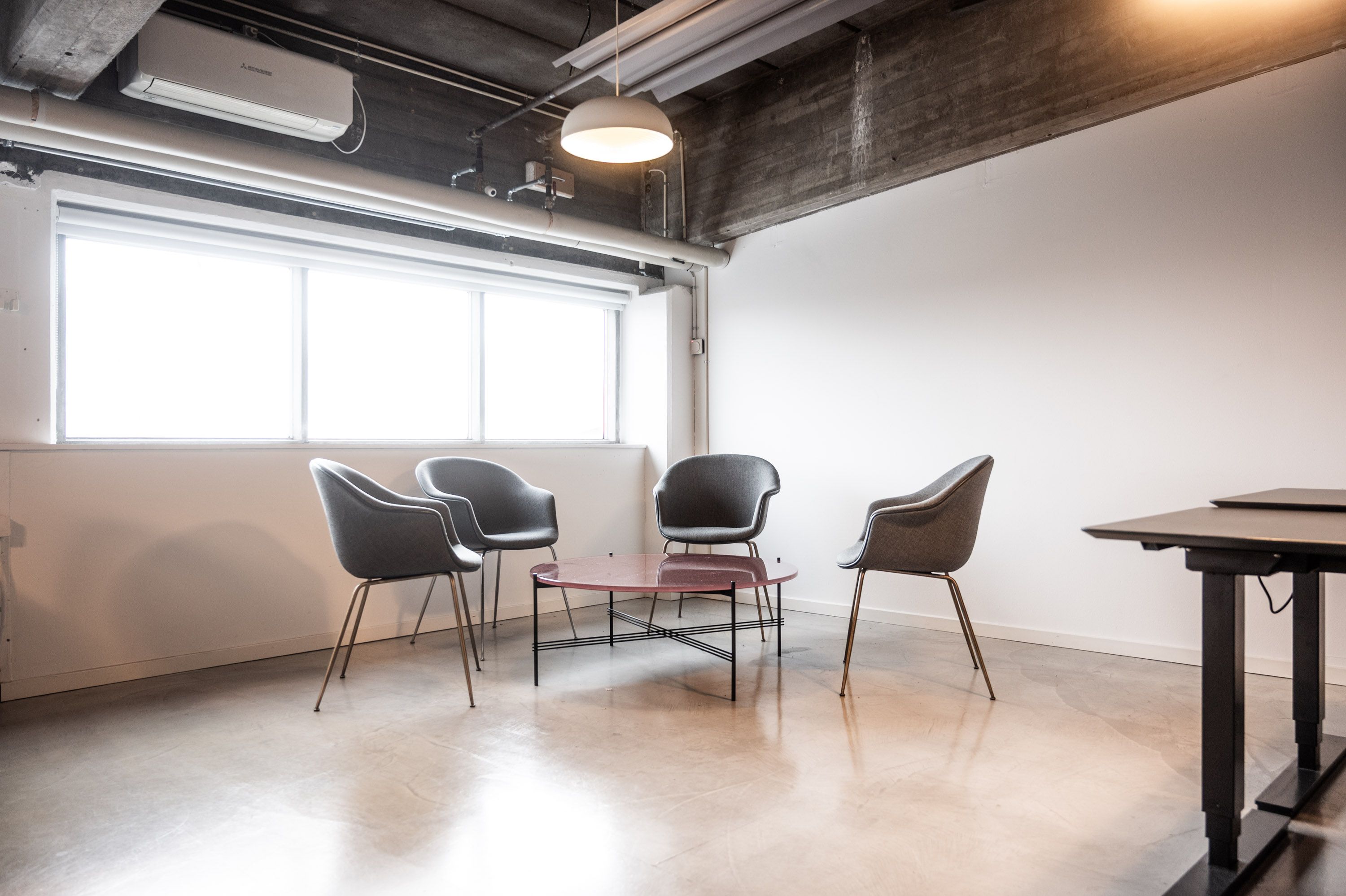 Moderne kontor med lyse tæpper og møbler, gulvtæppe, smukke stolpelampe, rekreativt område, glasvindue, klimaanlæg og skrivebord.