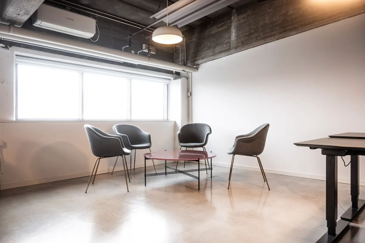 Moderne kontor med lyse tæpper og møbler, gulvtæppe, smukke stolpelampe, rekreativt område, glasvindue, klimaanlæg og skrivebord.