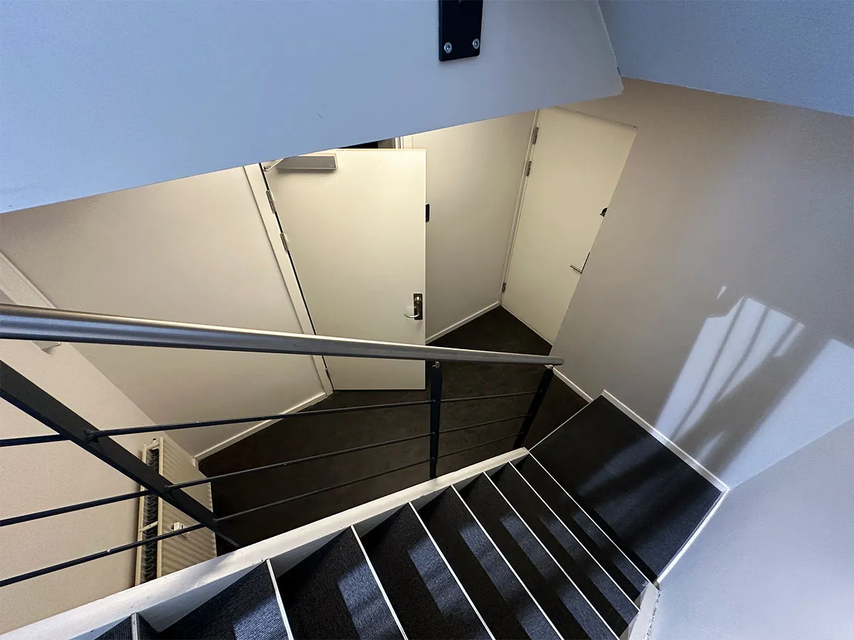 Moderne trappe med lyse og mørke trin og håndtag og en hvid dør på den øverste etage