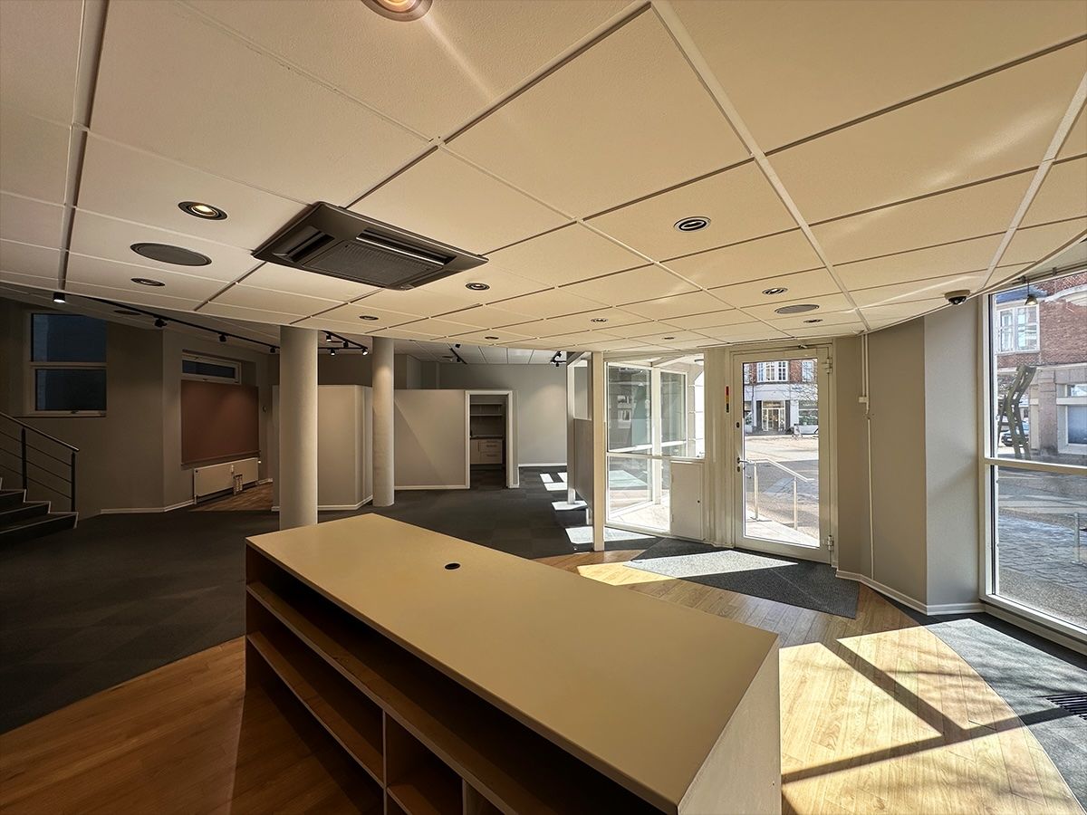 En stor lobby med højt loft og store glasruder med udsigt til gaden og parkerede biler