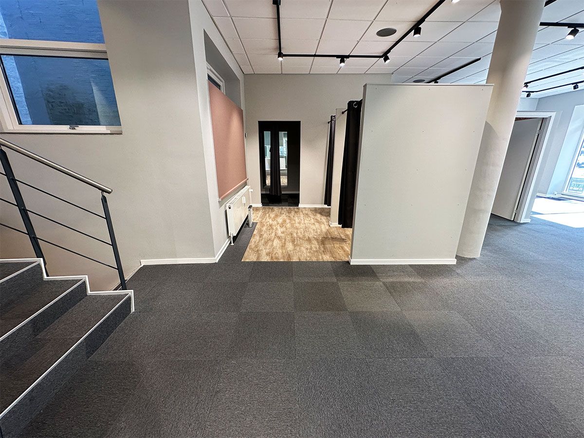 Foto af et lejlighedslejemål med trægulv og lyse vægge samt lyse gulvbelægning og lyse loftslys. Lokalet har et nyttige trappeopgang til næste etage