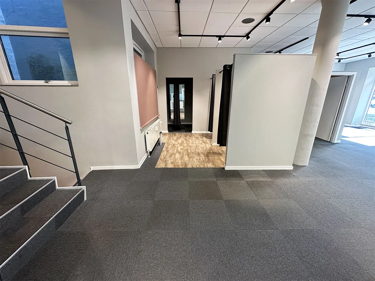 Foto af et lejlighedslejemål med trægulv og lyse vægge samt lyse gulvbelægning og lyse loftslys. Lokalet har et nyttige trappeopgang til næste etage