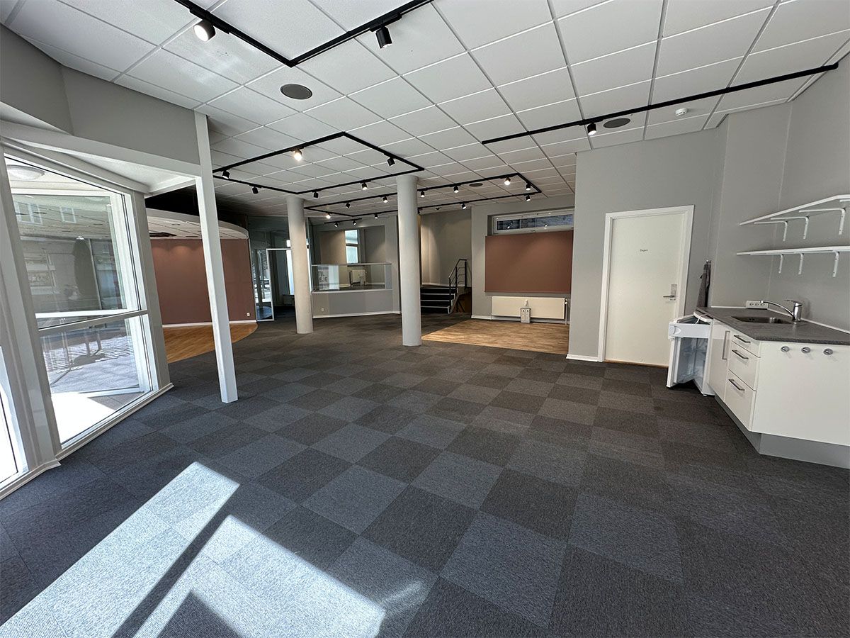 En stor og rummelig stue med højloft, hvide vægge og møbler med simpel design, hvor der er et åbent køkken med moderne møbler og lyse gulvbelægning