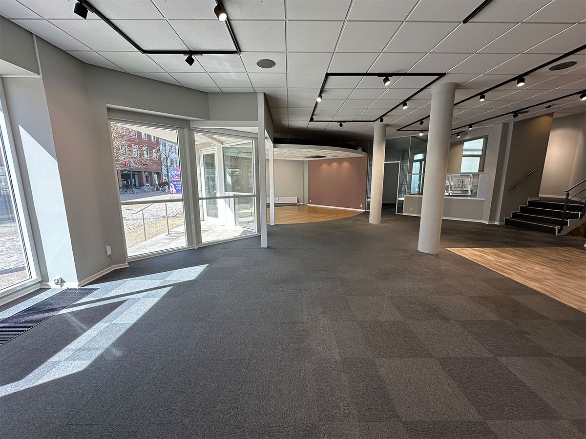 En tom og rummelig erhvervslokal i Hjørring med trægulv og glasvinduer mod en travl gågade med bygninger og cykler i baggrunden