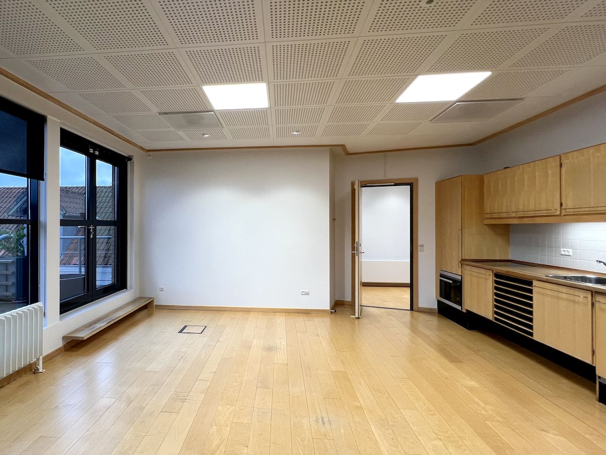 Et stort åbent kontor med lyse loftslamper, trægulv og hvid gardin og vindue i loftet