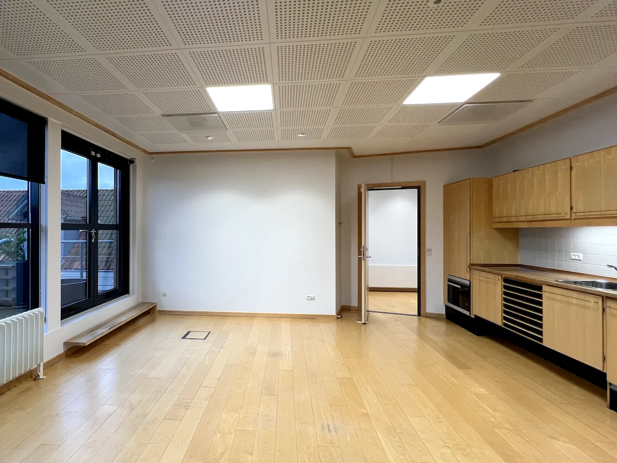 Et stort åbent kontor med lyse loftslamper, trægulv og hvid gardin og vindue i loftet