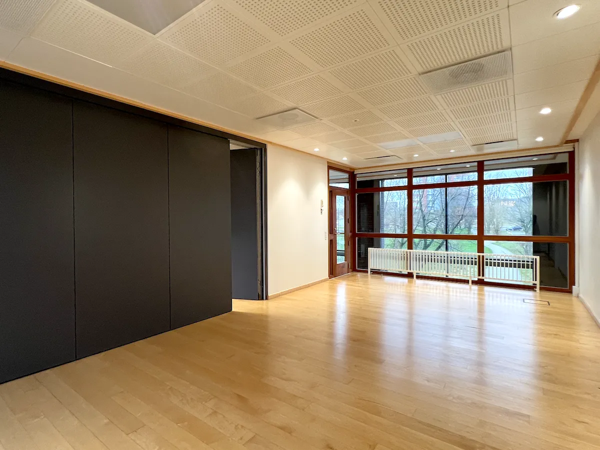 En stor, åben stue med trægulve og hvide vægge, store ruder og vinduesgardiner samt en skur og glasdør