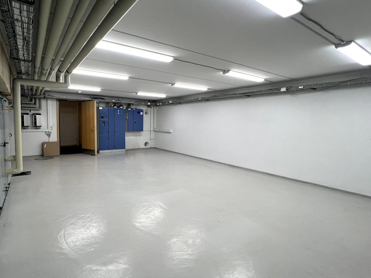 Moderne, åbent erhvervslokale med hvide vægge, højloft og lysarmaturer, hvor der er placeret kabinetter og døre.