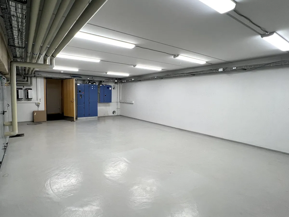 Moderne, åbent erhvervslokale med hvide vægge, højloft og lysarmaturer, hvor der er placeret kabinetter og døre.