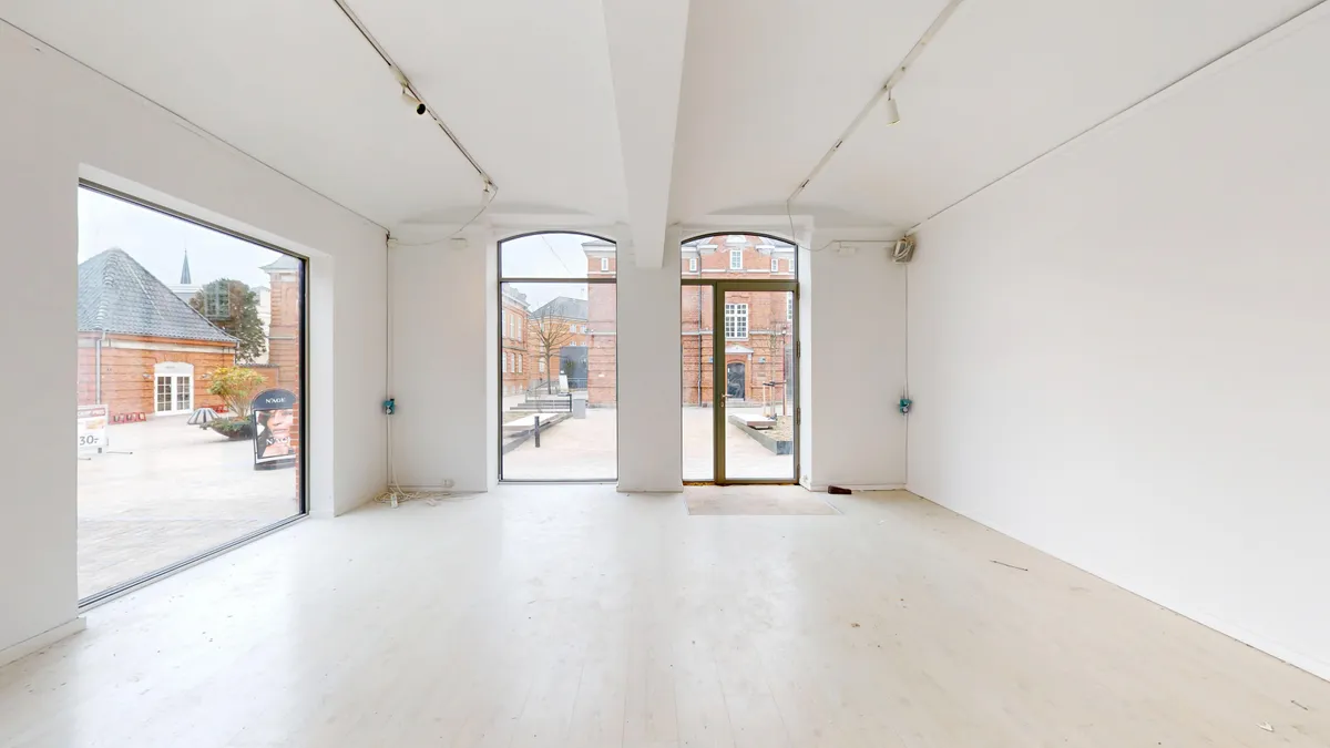 Lejlighed med moderne design og lyse vinduer til leje i København. Indeholder tre store glasdøre og en ren, hvid gulvbelægning.