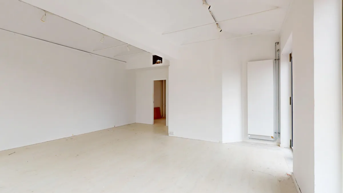 Et luksuriøst og rent lejemål med hvidvaskede vægge, en åben dør og en radiator. Der er et vindue med glas og et lysekron med flere lysepunkter. Gulvet er poleret og renset.