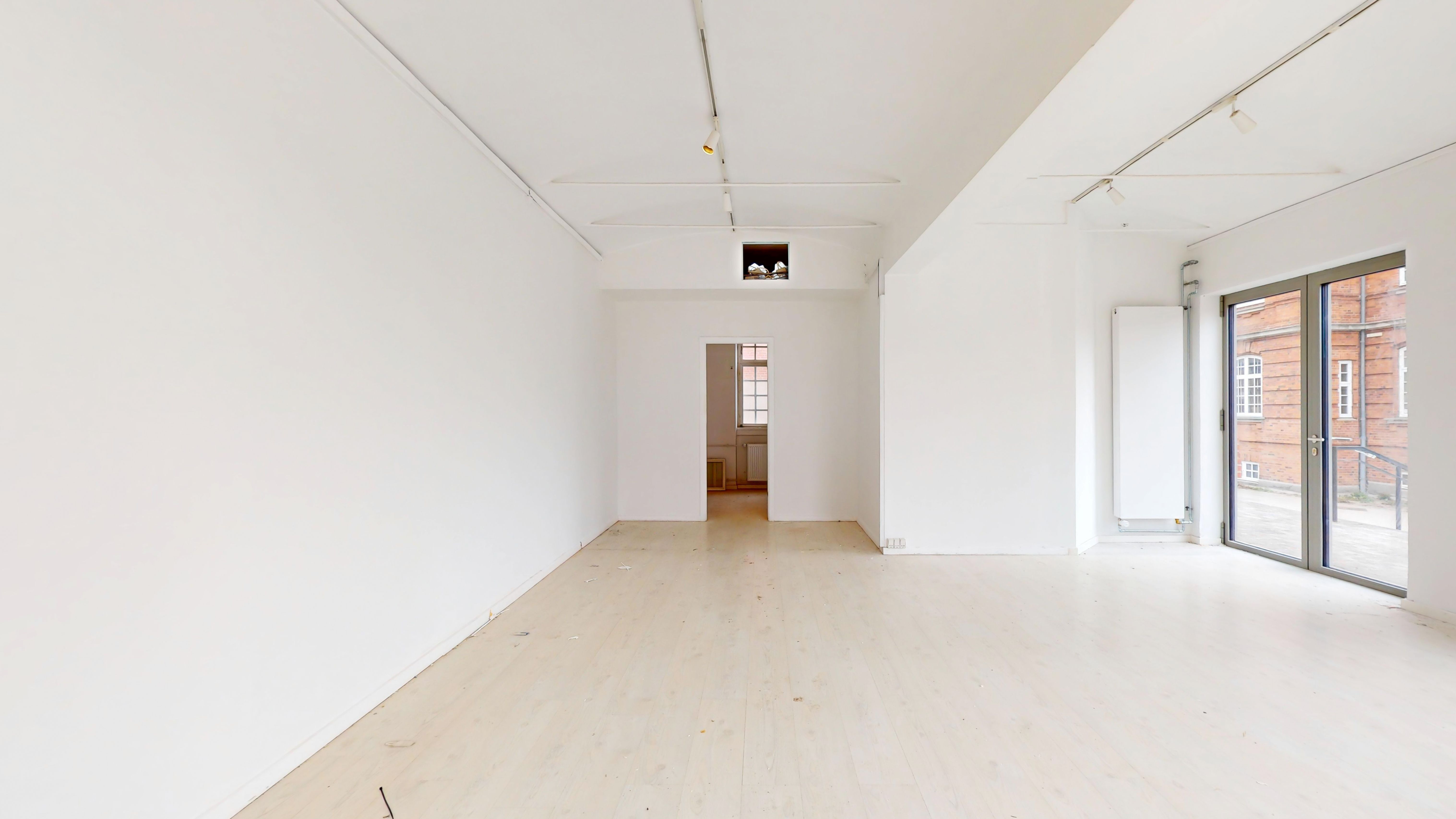 Et indbydende lejemål med hvide vægge, lyse gulve, to store vinduer og en dør i enden af rummet