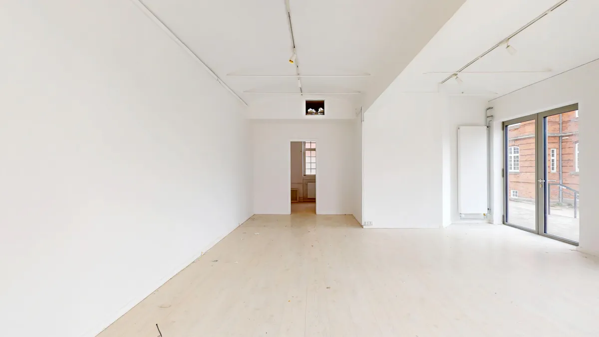 Et indbydende lejemål med hvide vægge, lyse gulve, to store vinduer og en dør i enden af rummet