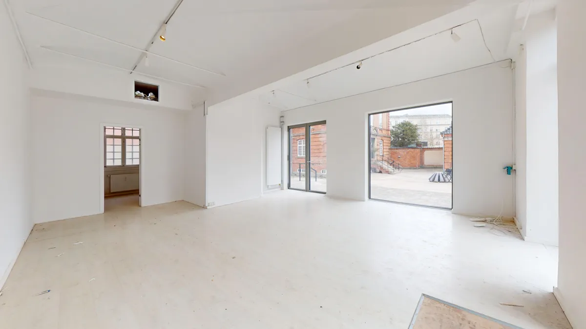 En tom lejlighed med lyse vægge, hvid gulv og store glasdøre med udsigt til gaden