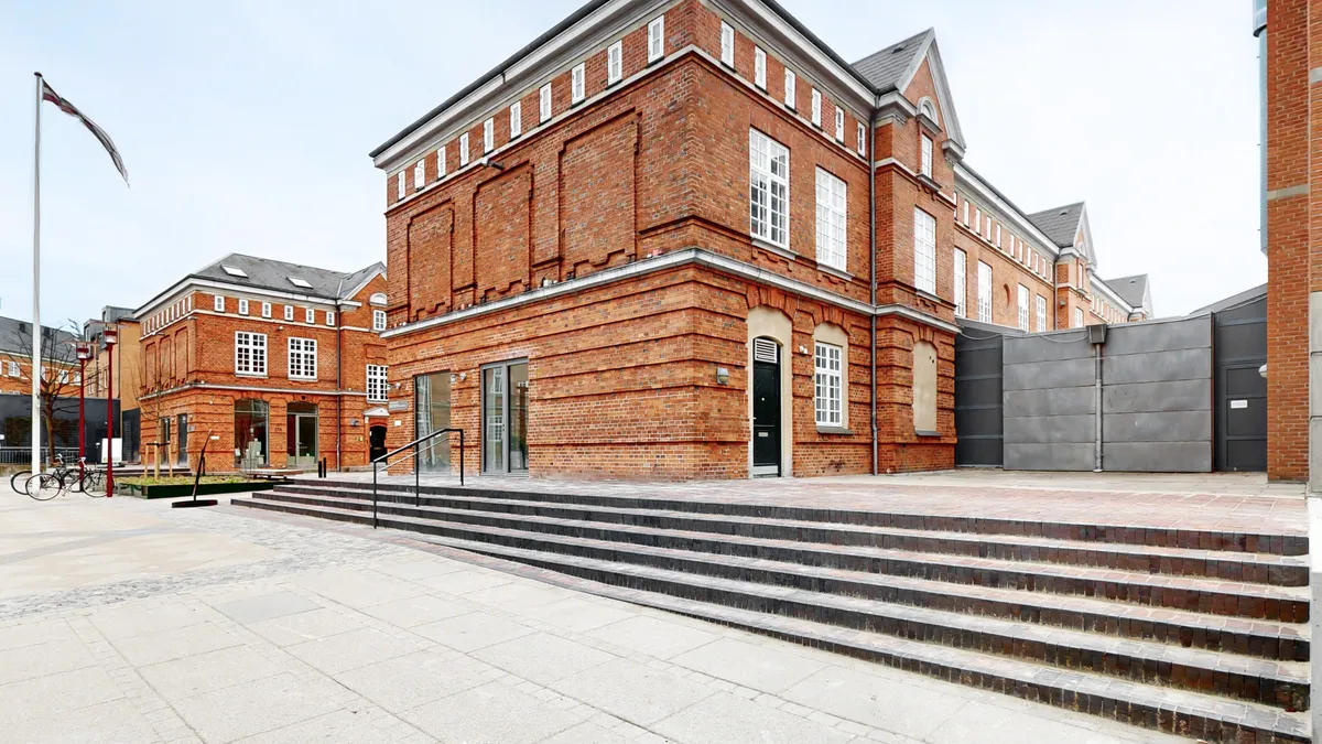 Lejemål på Østerfælled Torv med røde mursten, store vinduer, trapper og en flagpole med flag