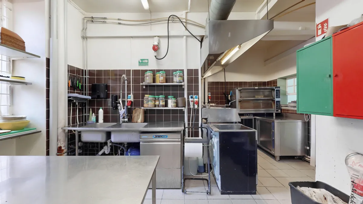 Et stort køkken med flere metalborde, en stålvask og en stor komfur i et lyserødt og grønt farveskema