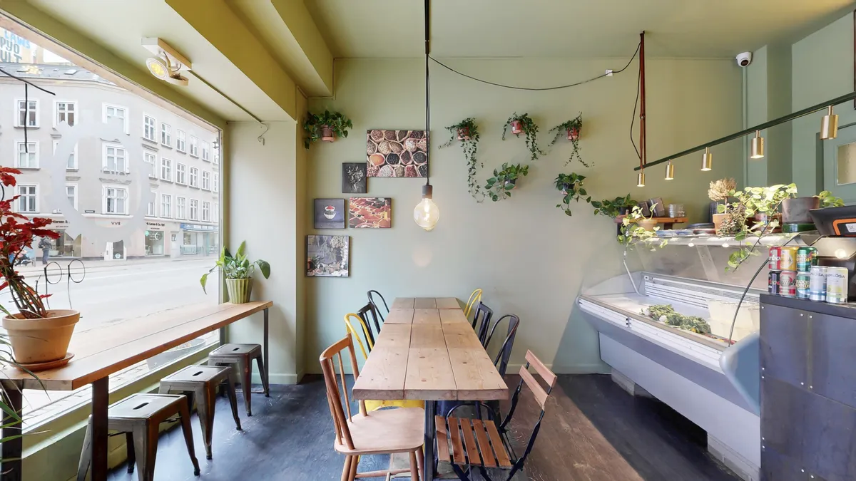 Lys og lyse interiør med lysegule vægge, bord og stole og plantepot i lysebrun jordfarve. Gulv og vægge er lavet af træ.